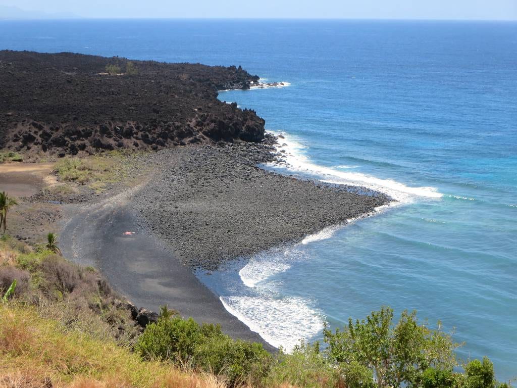Black solidified lava flows spilling down a bare volcanic slope toward the coast