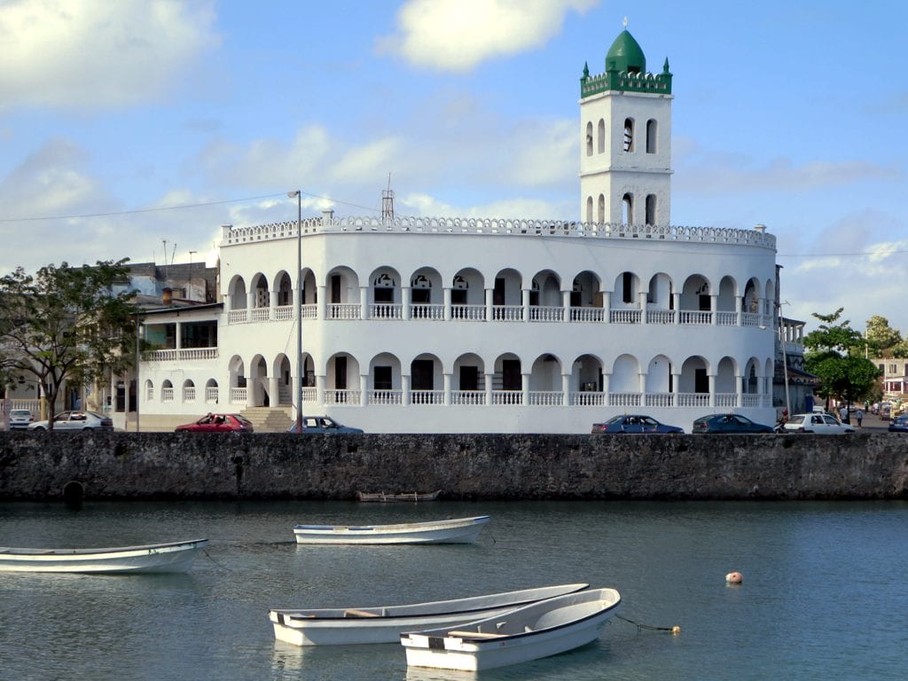 A white mosque with a low minaret directly on a stone sea wall, waves below