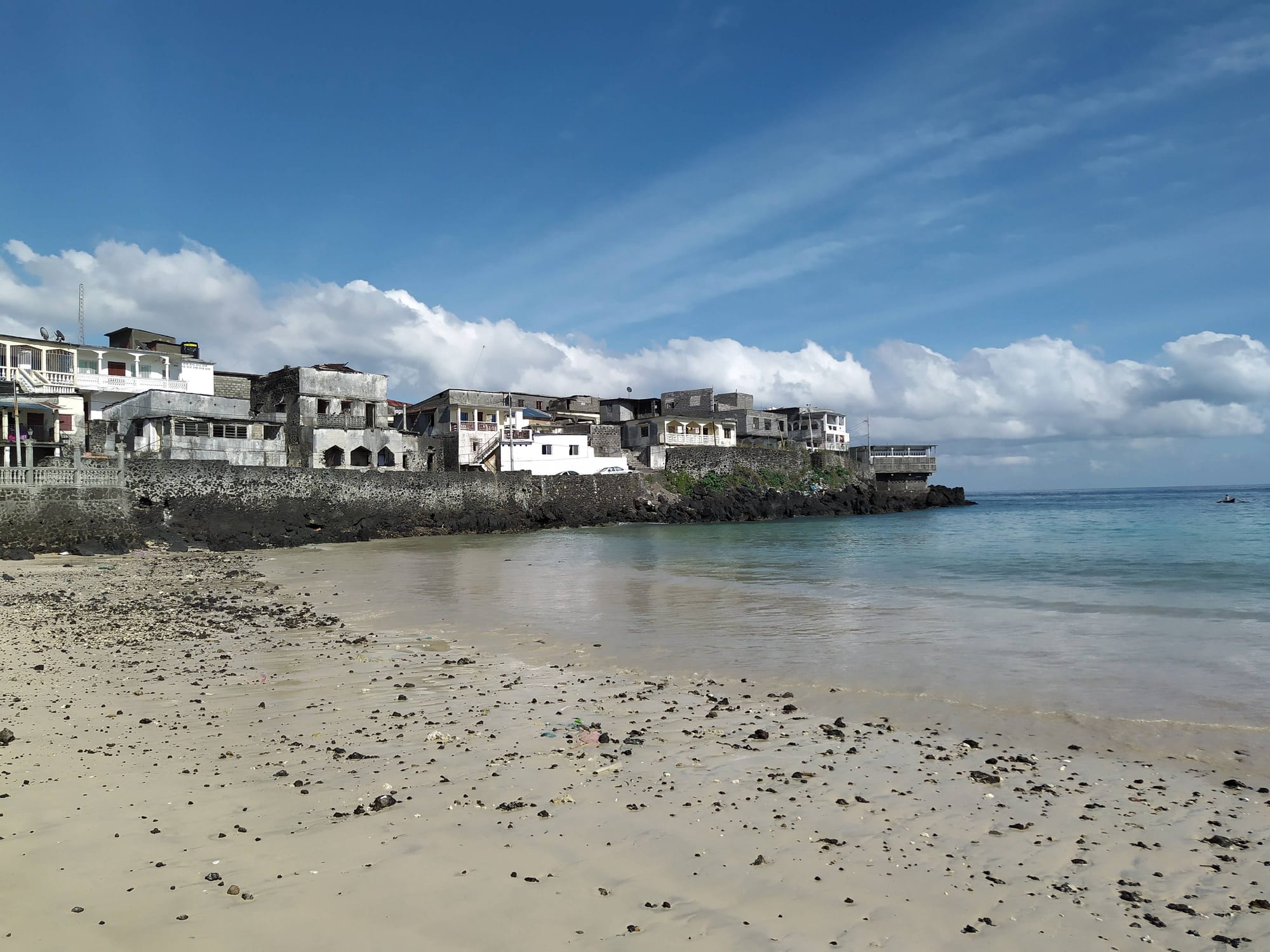 A rocky black-sand shore with fishing pirogues and the town behind
