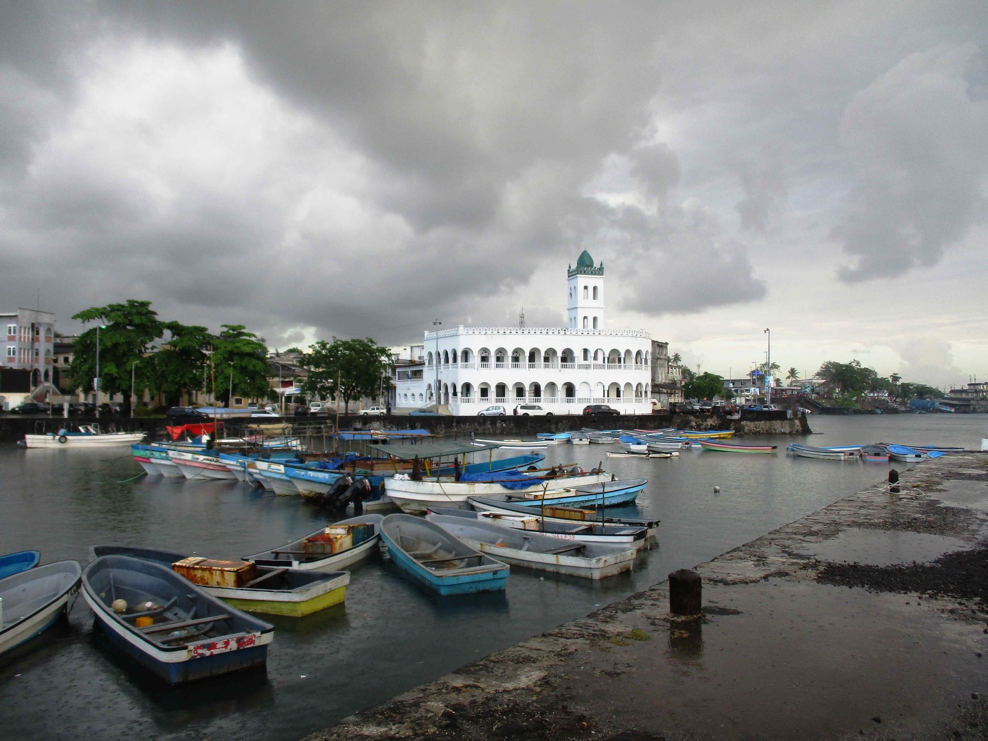 A white coral-stone mosque with a square minaret and arcaded galleries on a rocky seafront