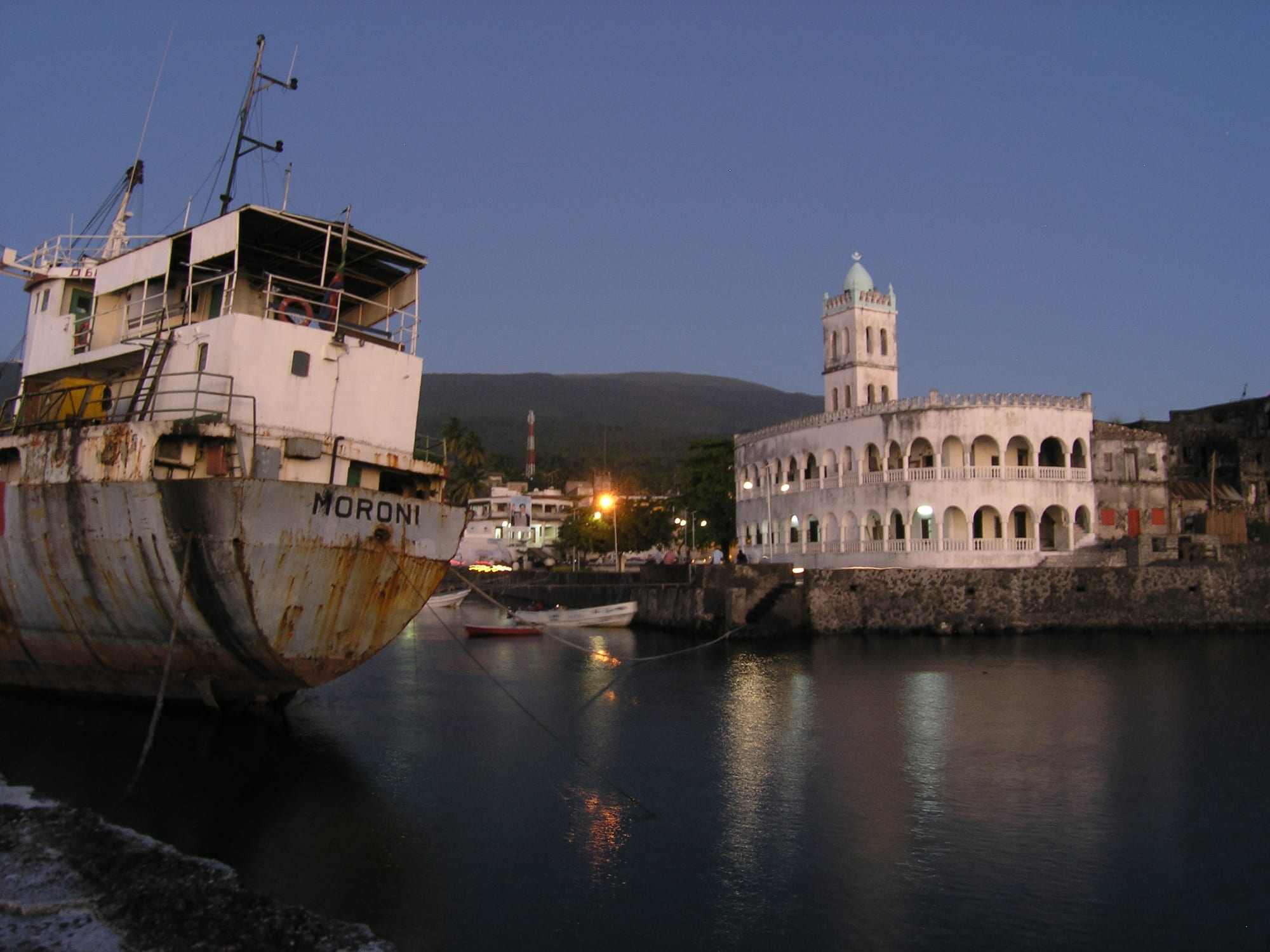 A white mosque with slender minarets on the waterfront of a small tropical capital, dhows in the bay