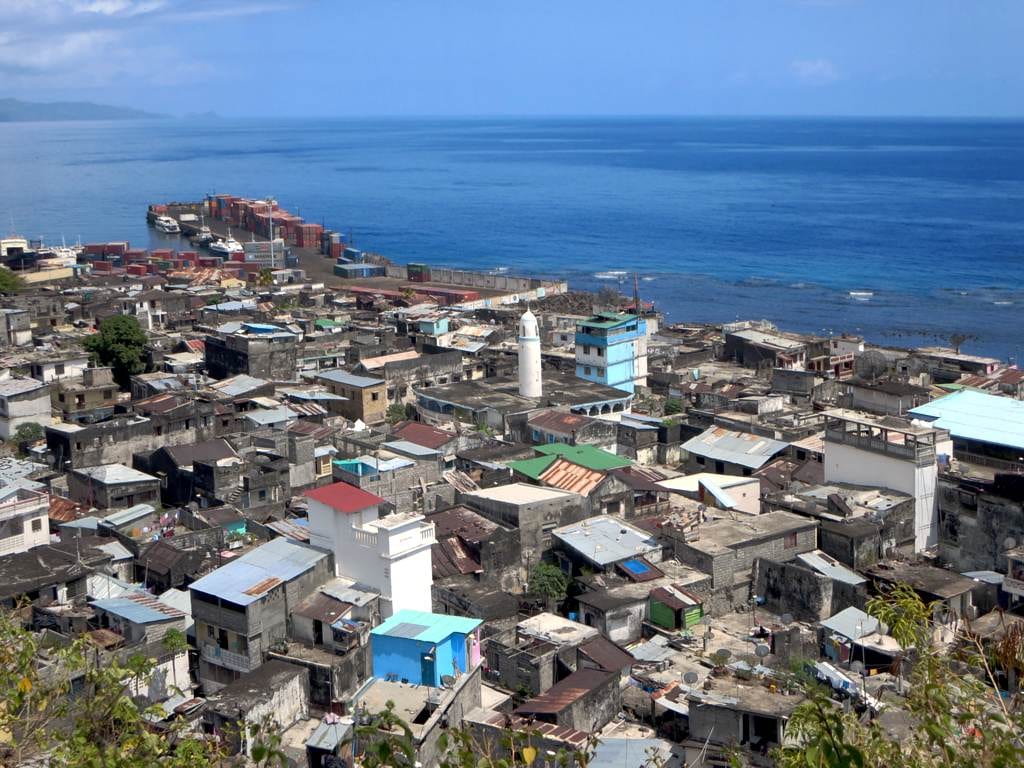 Narrow lanes of tall weathered stone and coral houses climbing a hillside above a small port