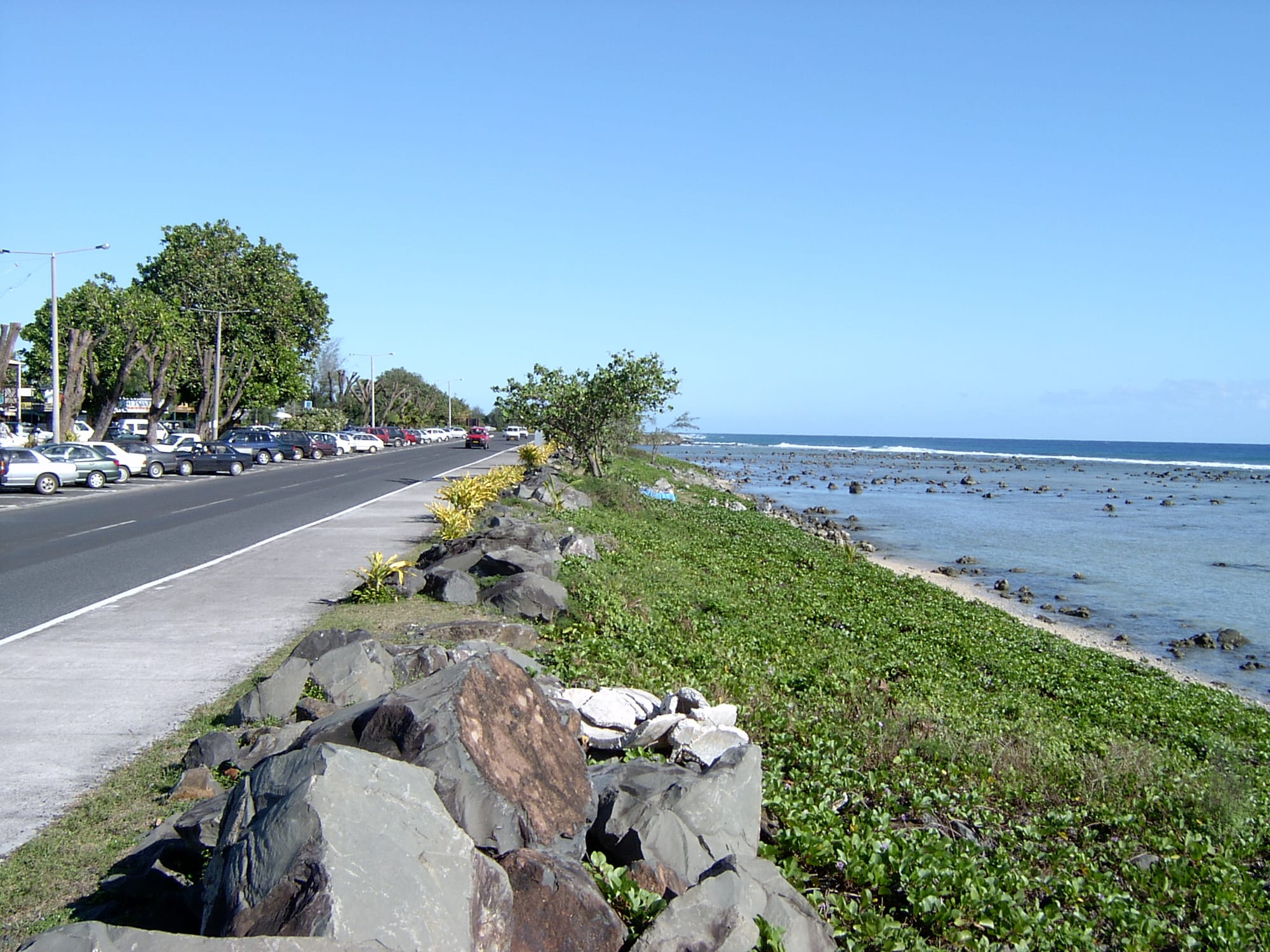 A low seafront town of small buildings and palms along a reef-fringed coast under a green volcanic ridge