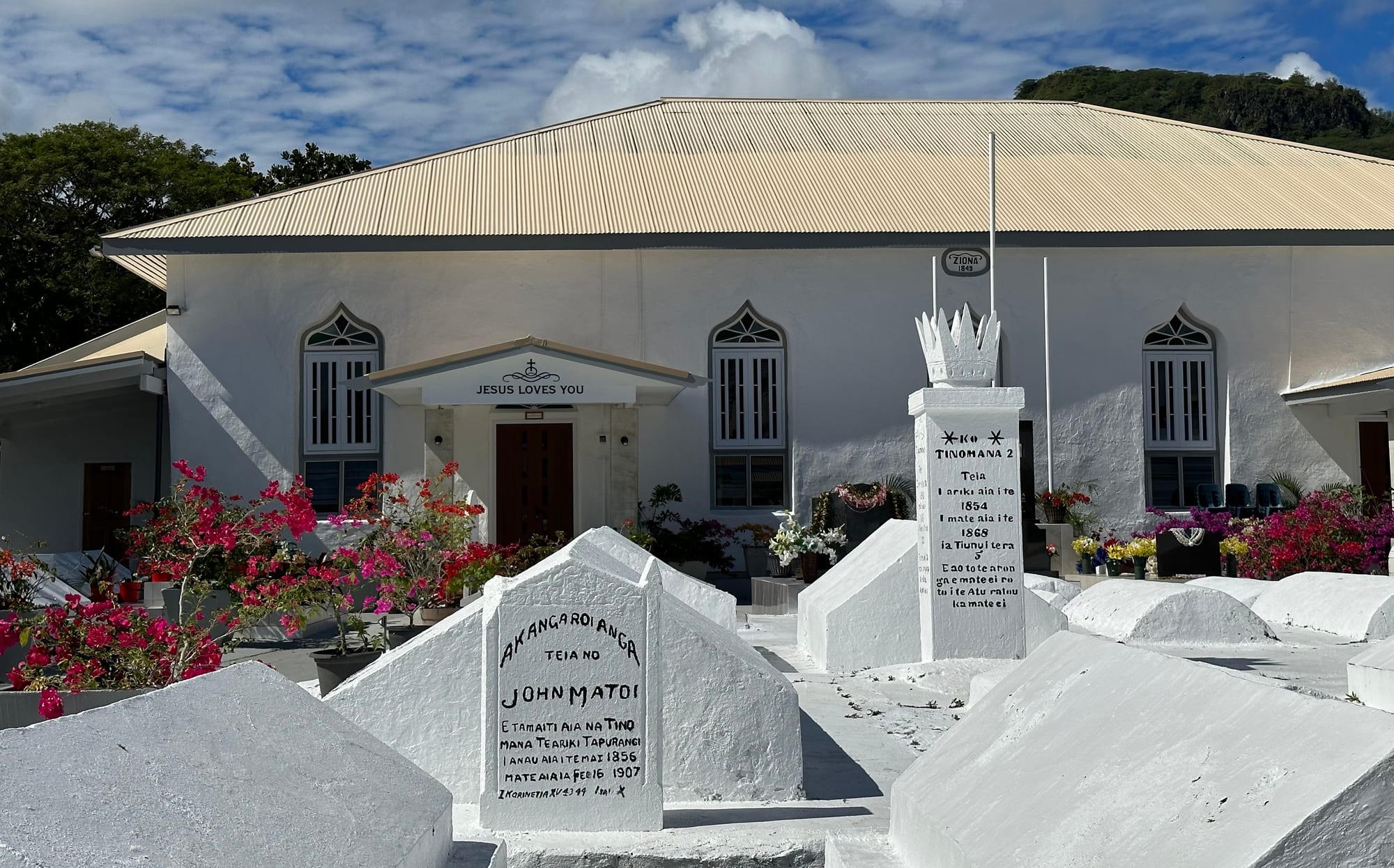 A whitewashed church with arched windows and a flower-filled churchyard containing whitewashed grave monuments