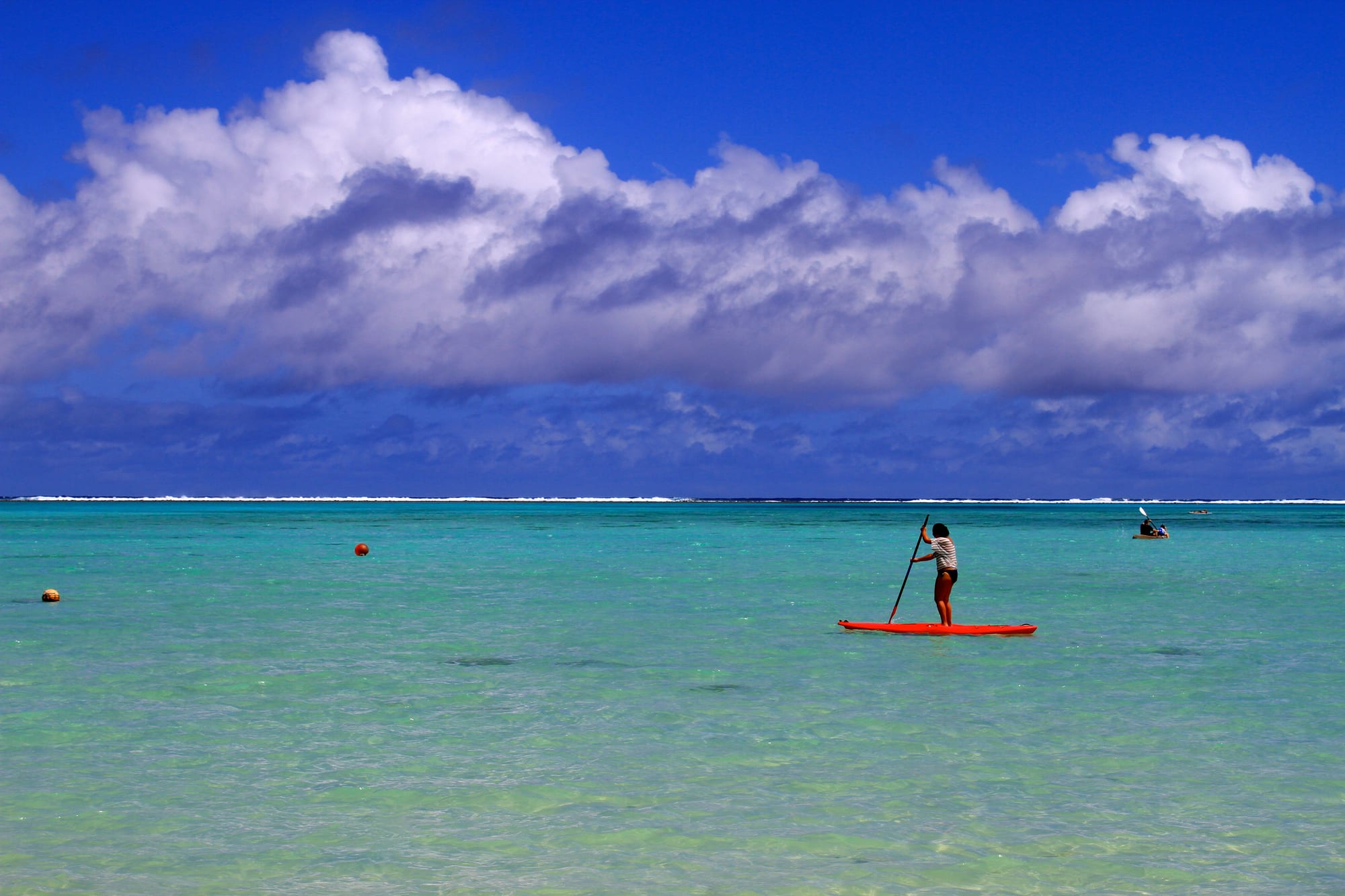 A calm shallow lagoon with small green islets, palms leaning over pale sand