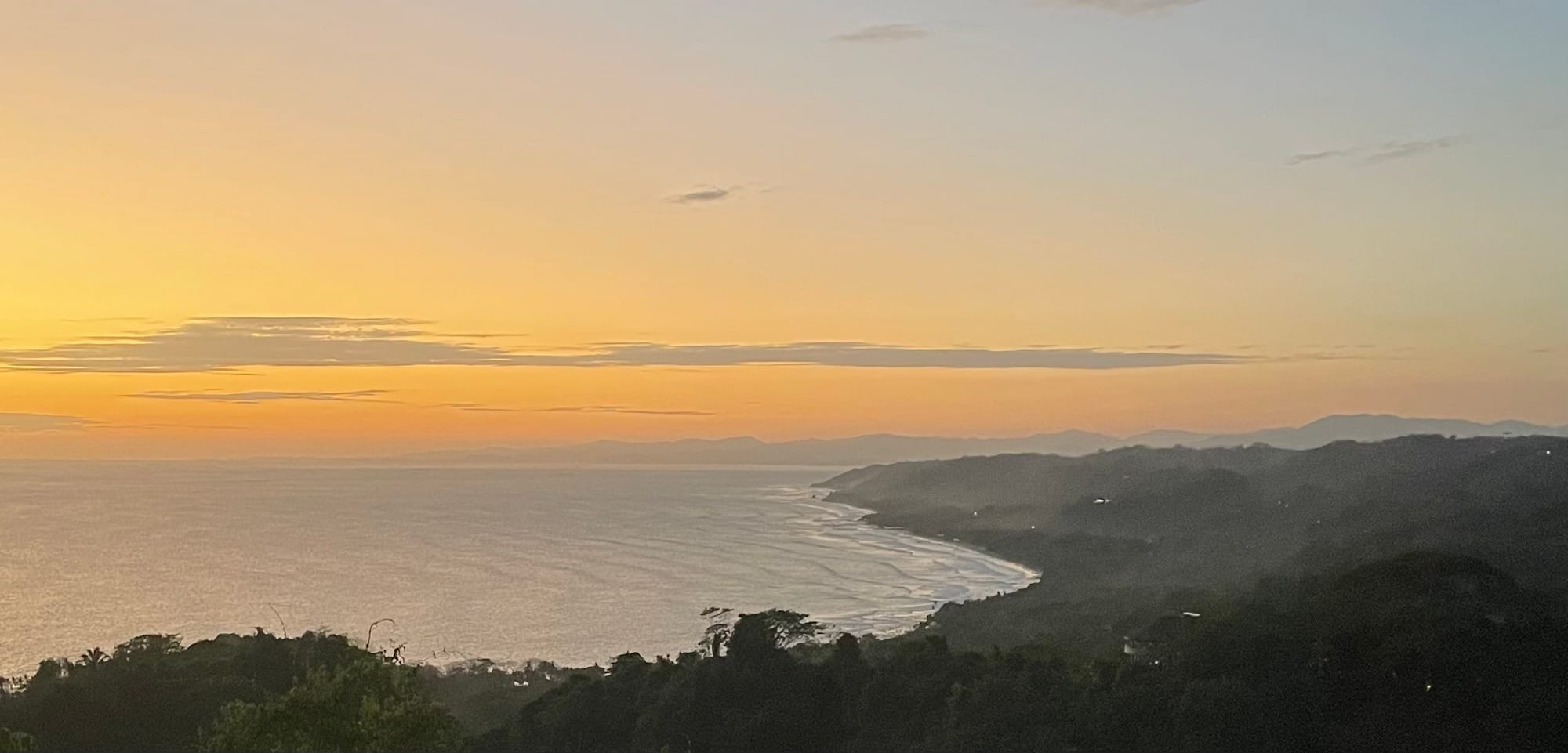A long Pacific beach with surf, driftwood, and jungle-covered hills behind