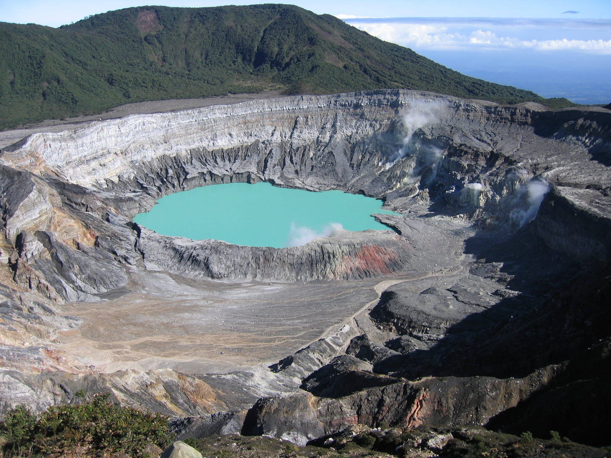 A vast steaming crater with a pale acid-green lake at the bottom