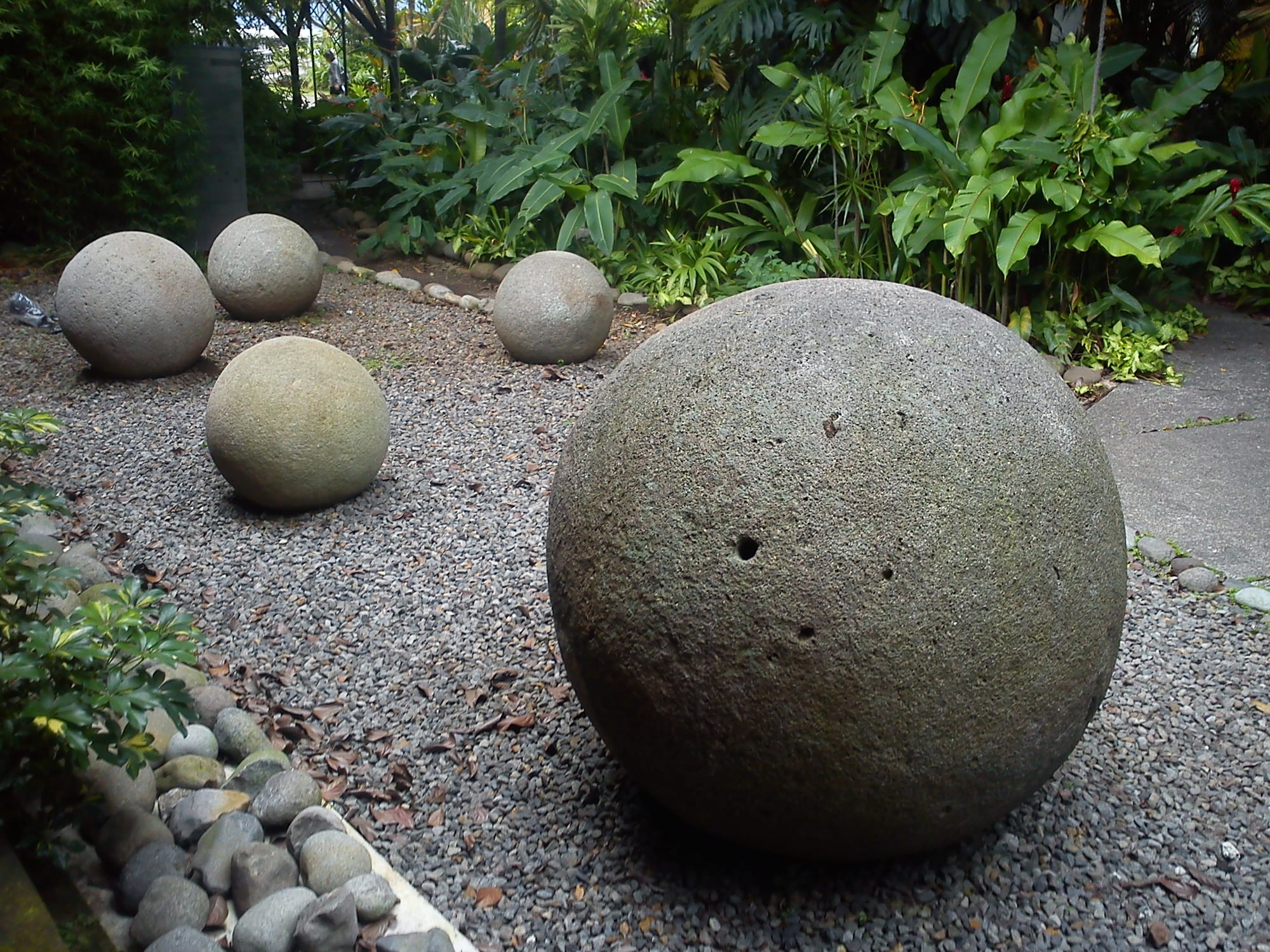 Several large, almost perfectly round grey stone balls of different sizes on a grass lawn