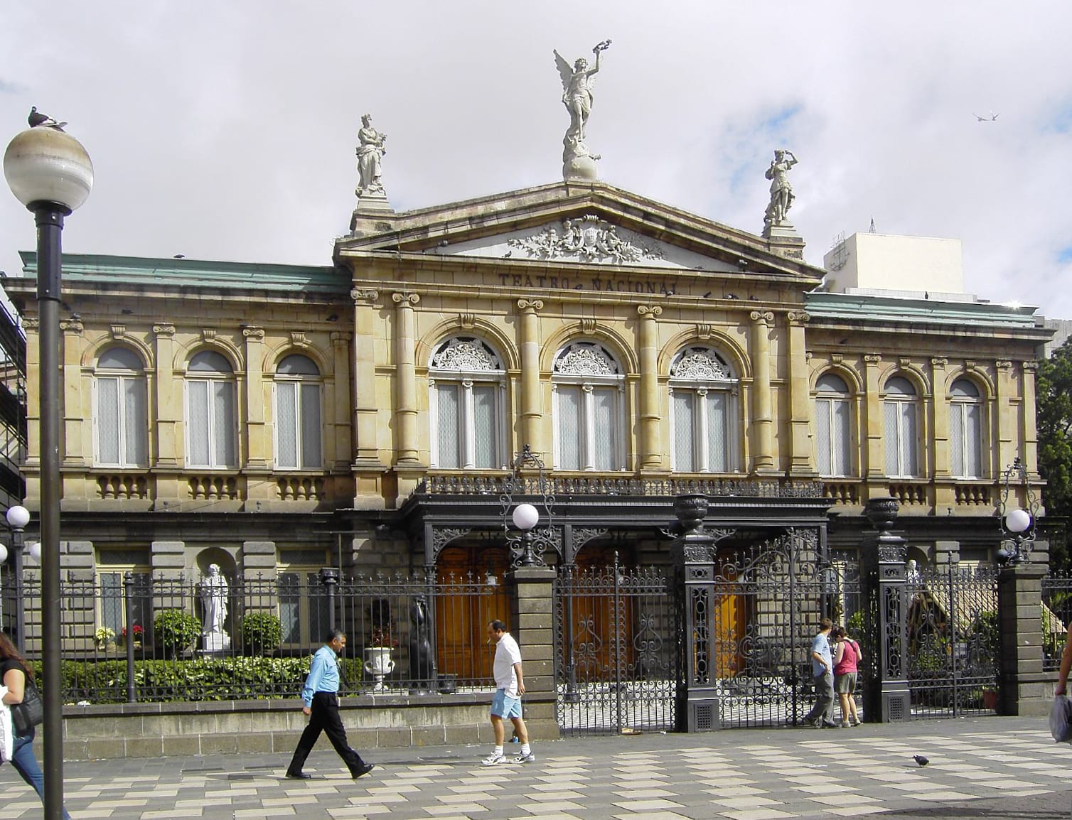 An ornate neoclassical theatre with a columned portico and statues, in a city plaza