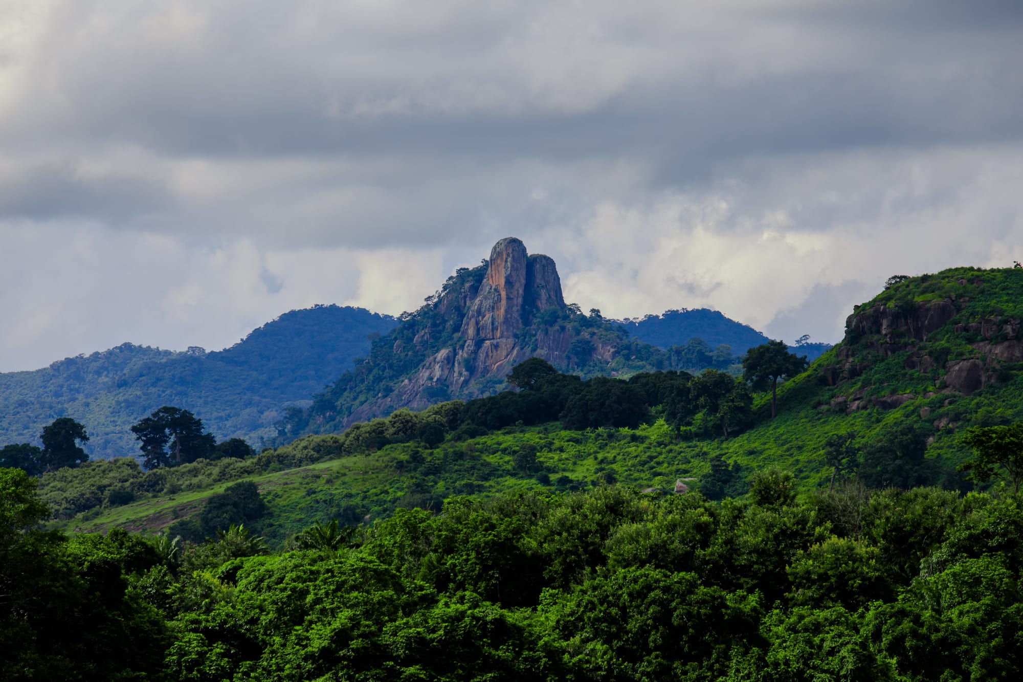 A sharp tooth-shaped forested mountain rising above rolling green hills