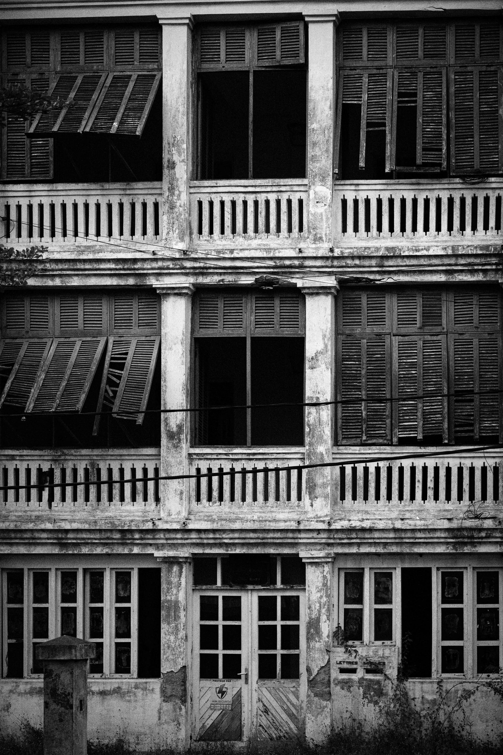 A weathered two-storey French colonial building with shuttered arcades and a balcony, among palms