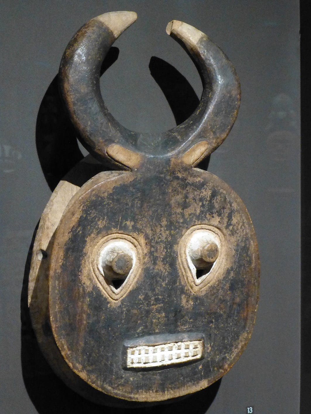 A large round wooden mask painted in blocks of colour with a curved horn form, from the Baoulé people