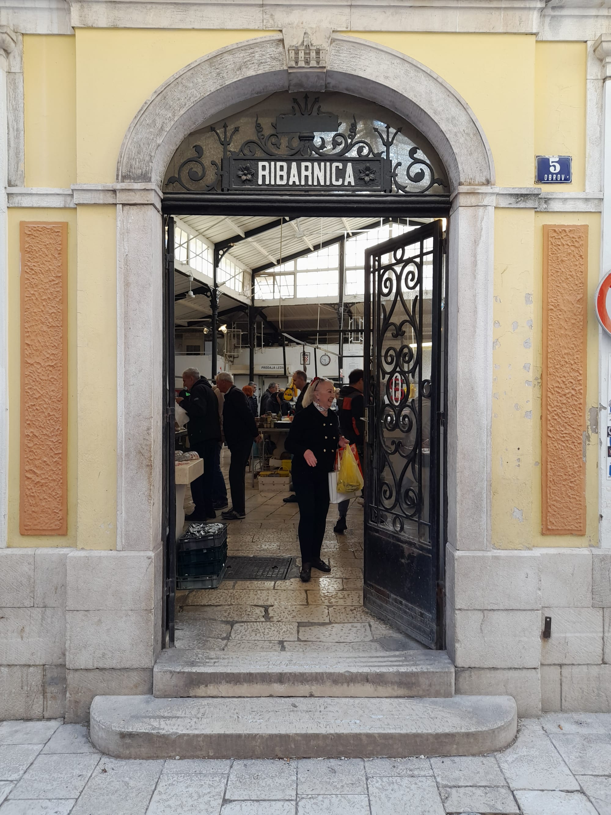 People at a covered fish market stall in Split, with fish laid out for sale under an arched stone entrance