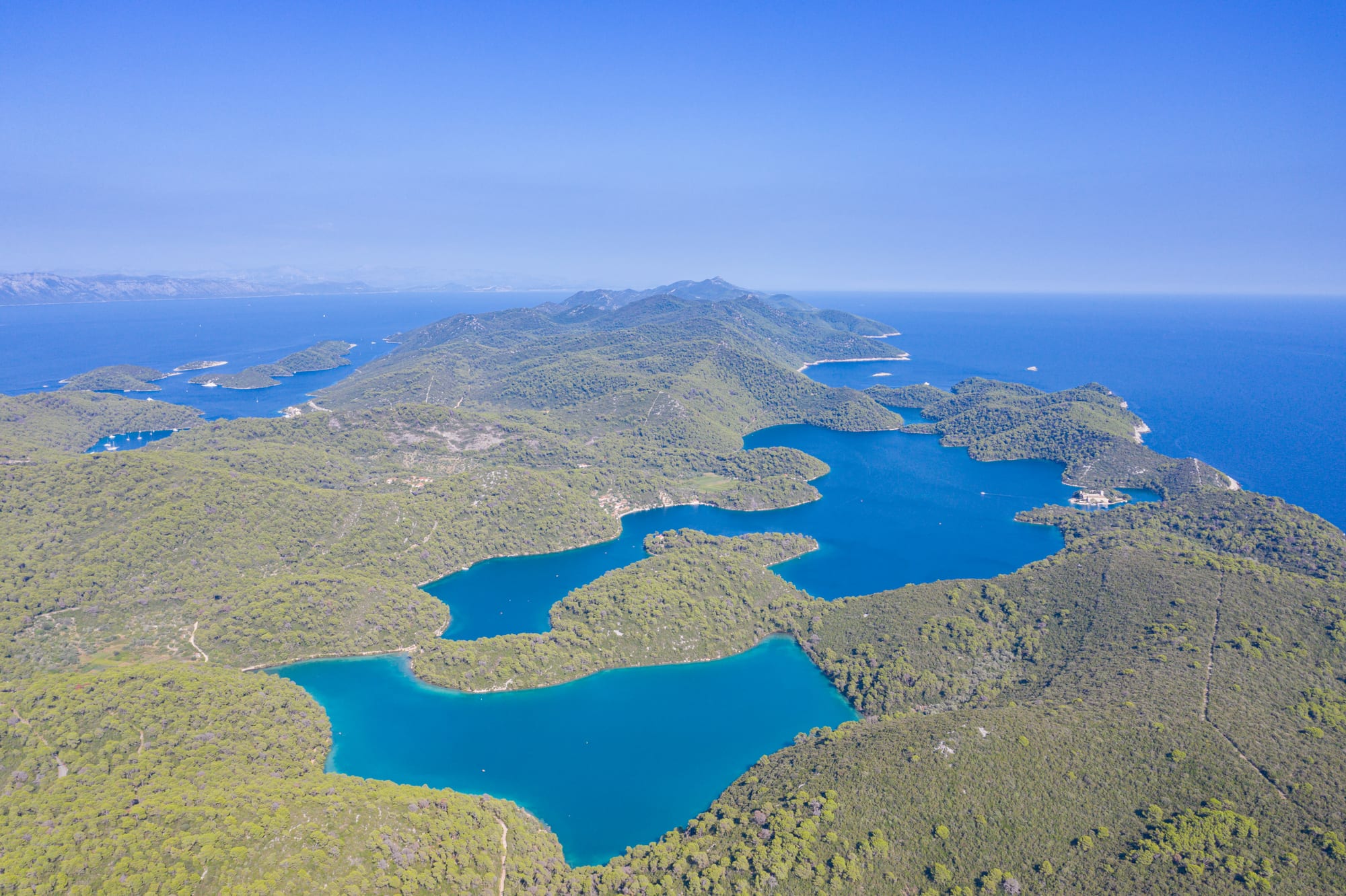 Two connected saltwater lakes ringed by pine forest, a small island with a monastery in one