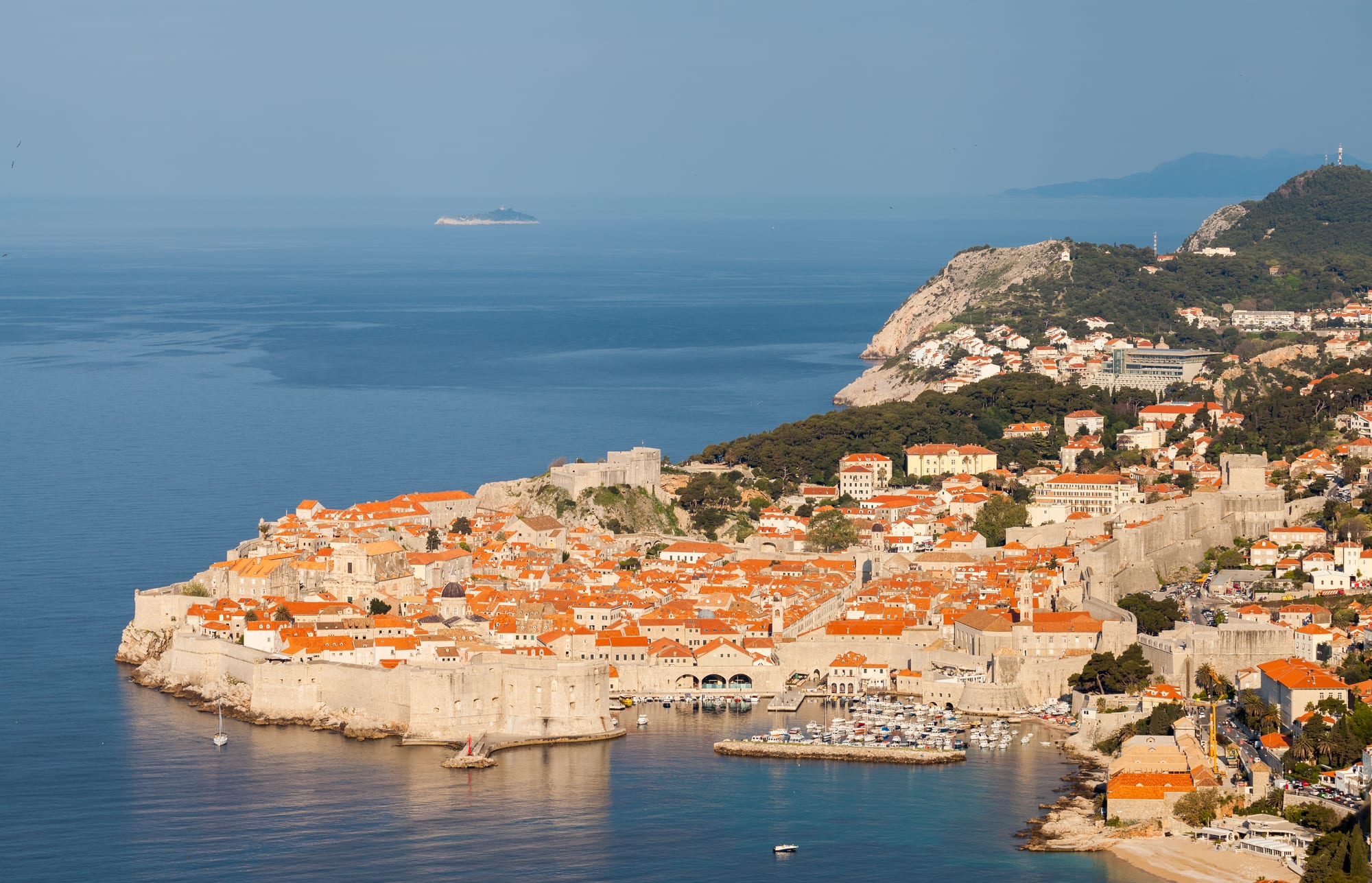 A view along the top of massive city walls, terracotta roofs below, sea beyond