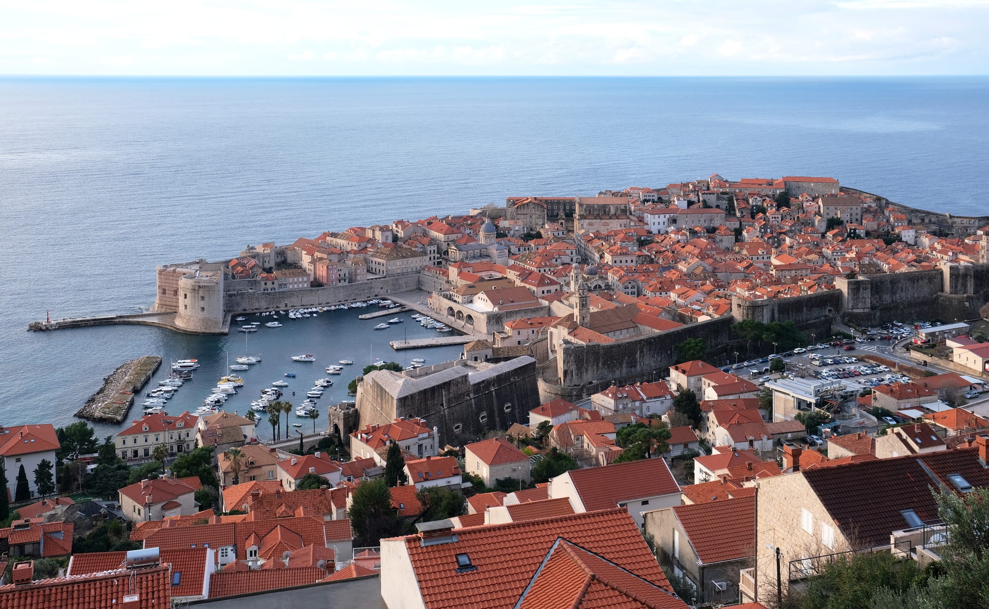A walled medieval city of terracotta roofs on a headland jutting into a deep blue sea