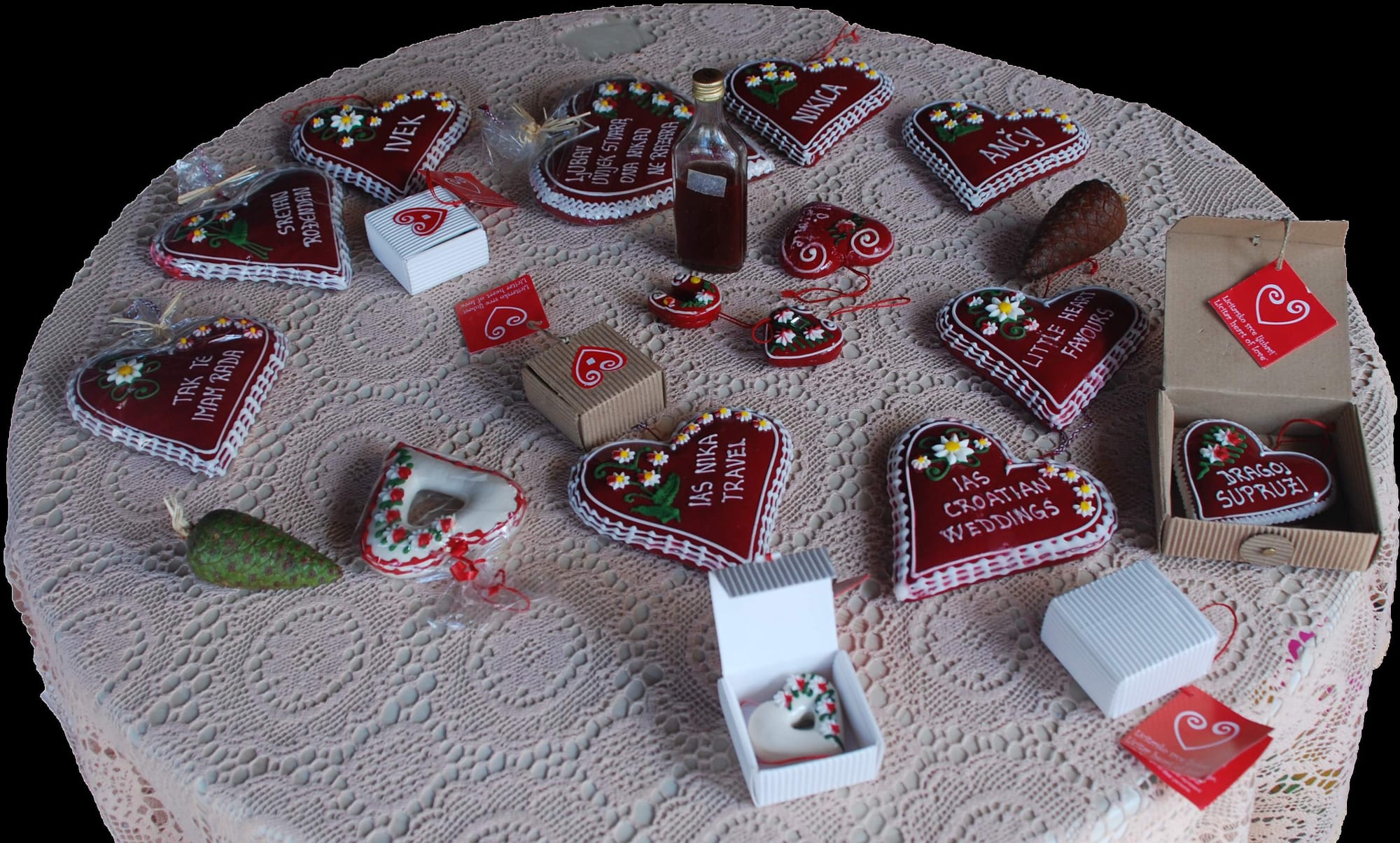 Red heart-shaped gingerbread biscuits decorated with white piping, flowers and hand-lettered names and messages, laid out on a lace tablecloth