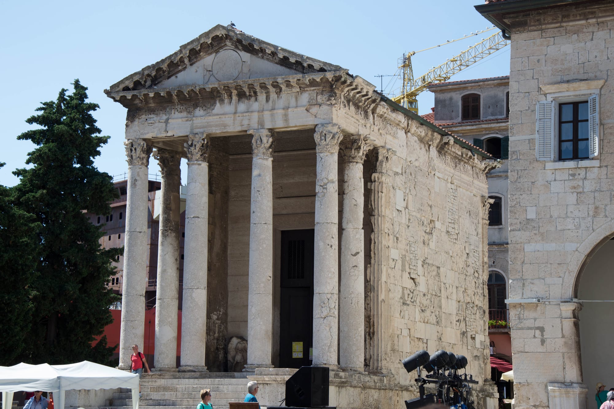 A small Roman temple with a porch of tall Corinthian columns and a triangular pediment, standing on a town square