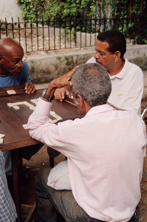 Three men gathered around a wooden table playing dominoes on a Havana street