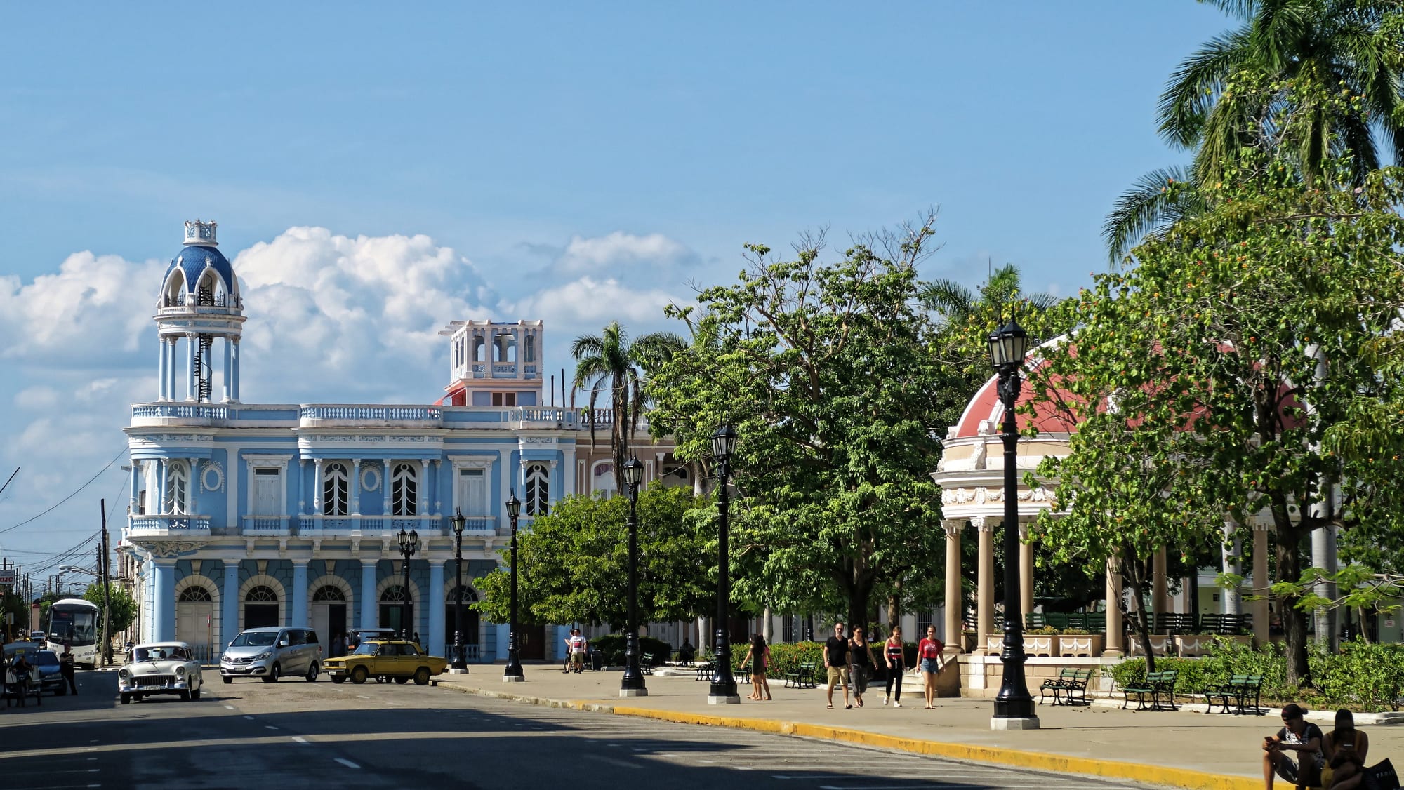 A formal palm-lined plaza framed by neoclassical buildings with a domed theatre