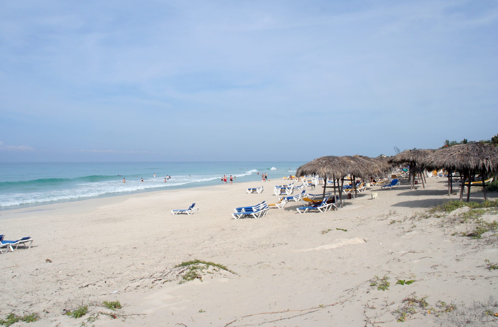 A long white-sand beach lined with palm trees, calm turquoise water beyond