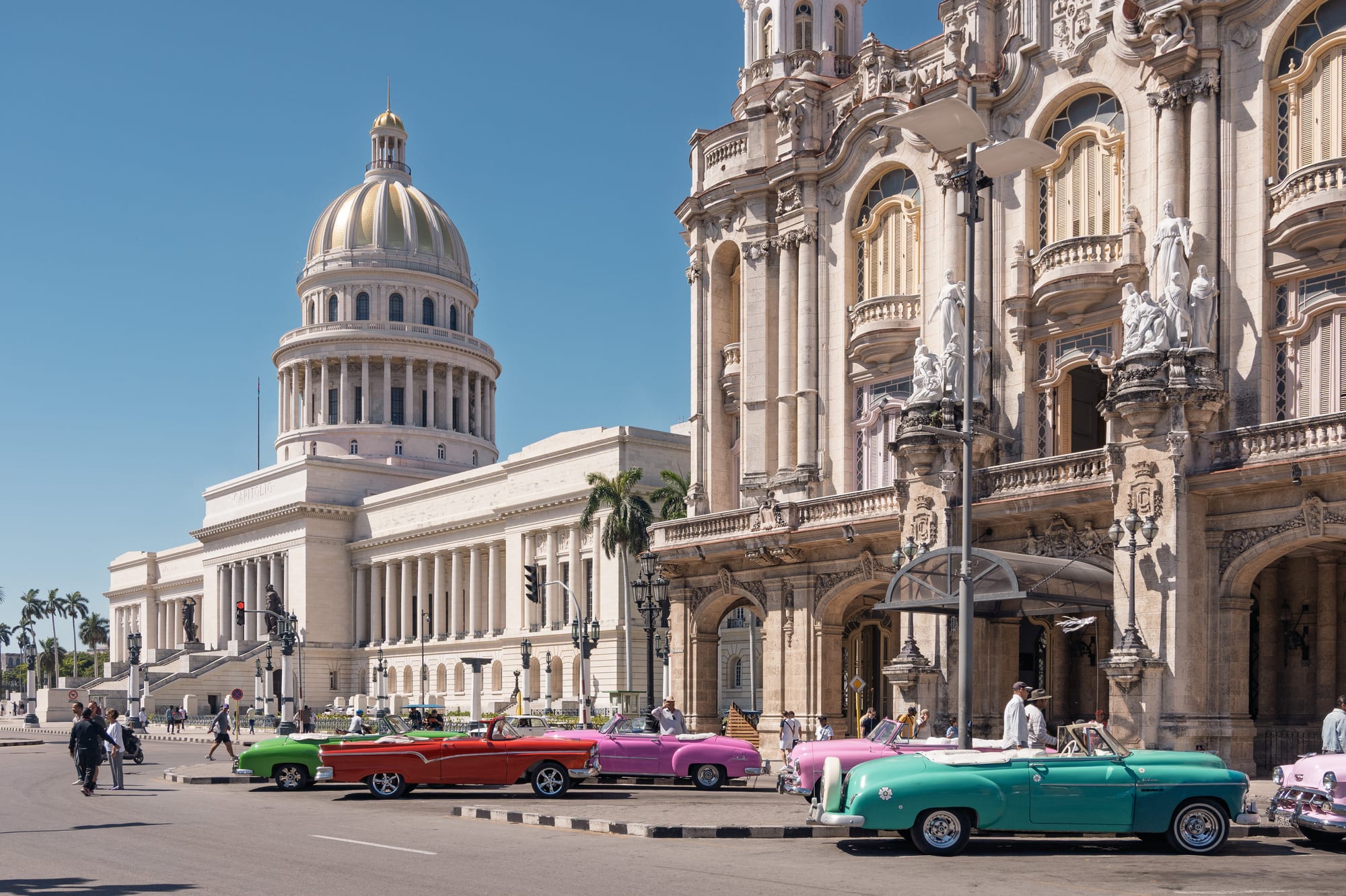A domed capitol building behind a row of parked 1950s American convertibles