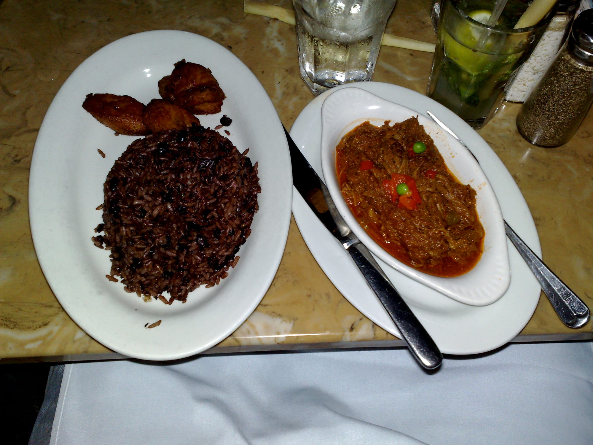 Two plates, one with rice and black beans and fried plantain, the other with shredded beef in tomato sauce