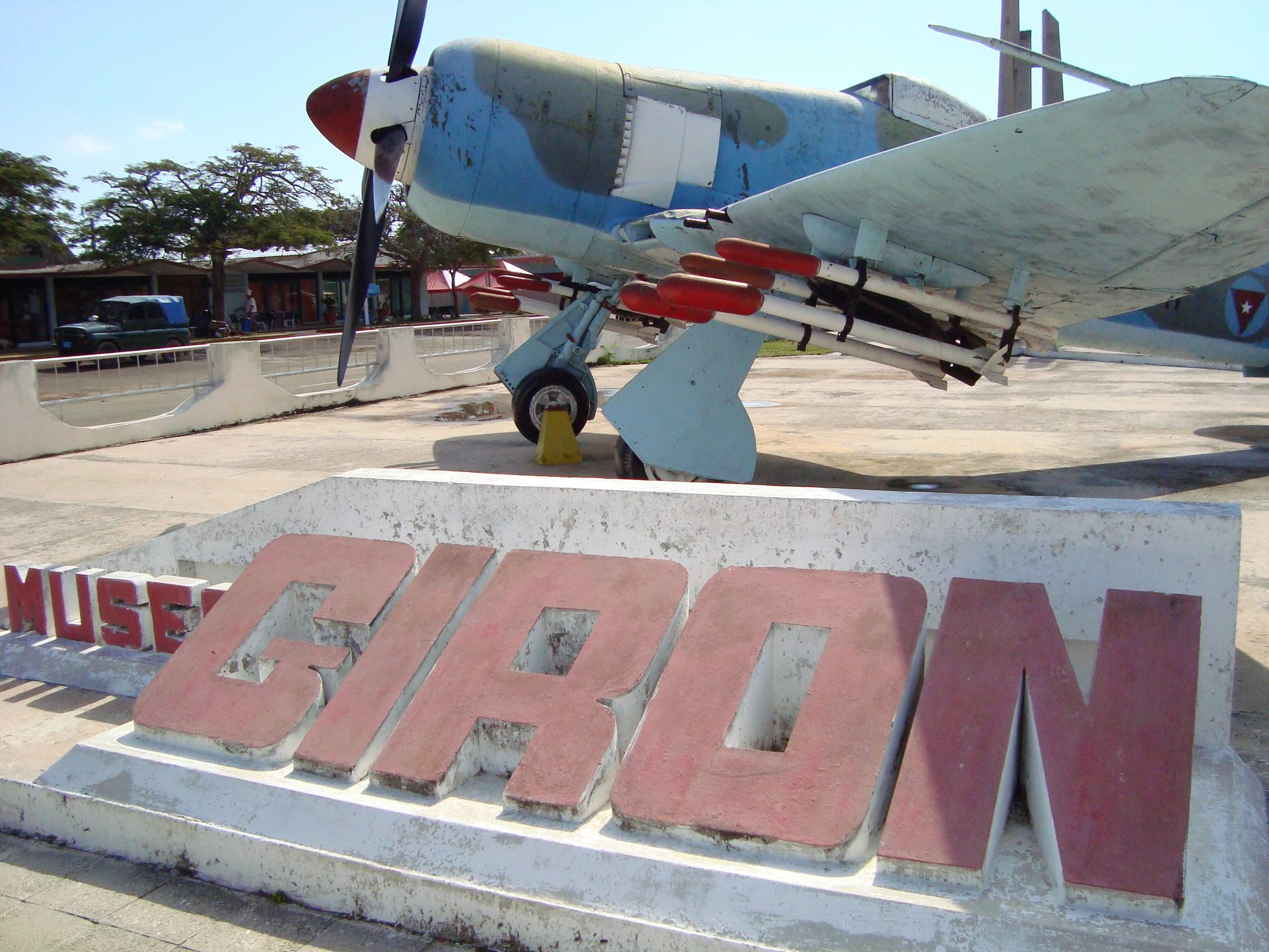 An old propeller warplane on a plinth beside a sign reading Museo Girón