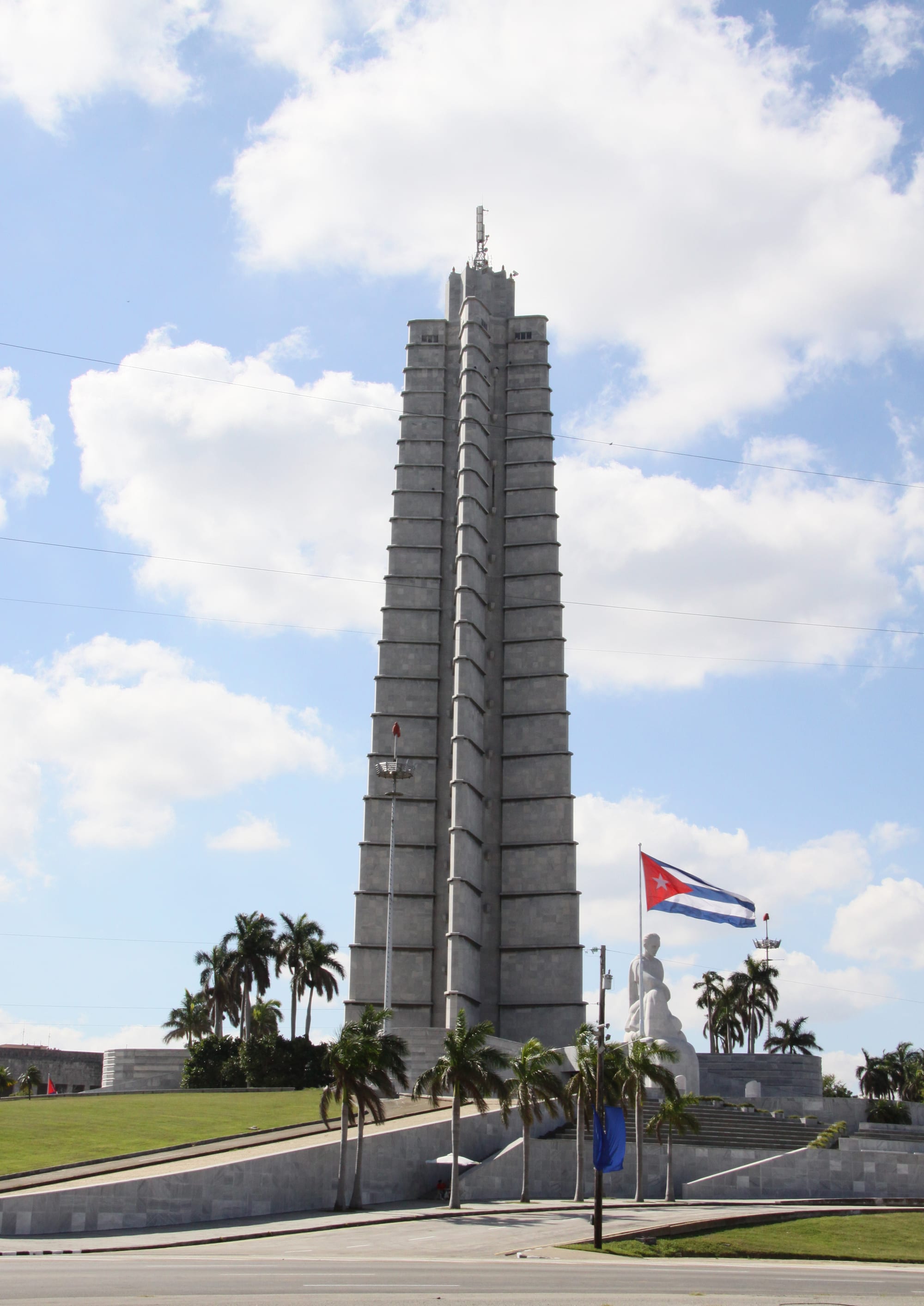 A tall grey star-shaped stone tower and a white marble seated statue on a huge plaza