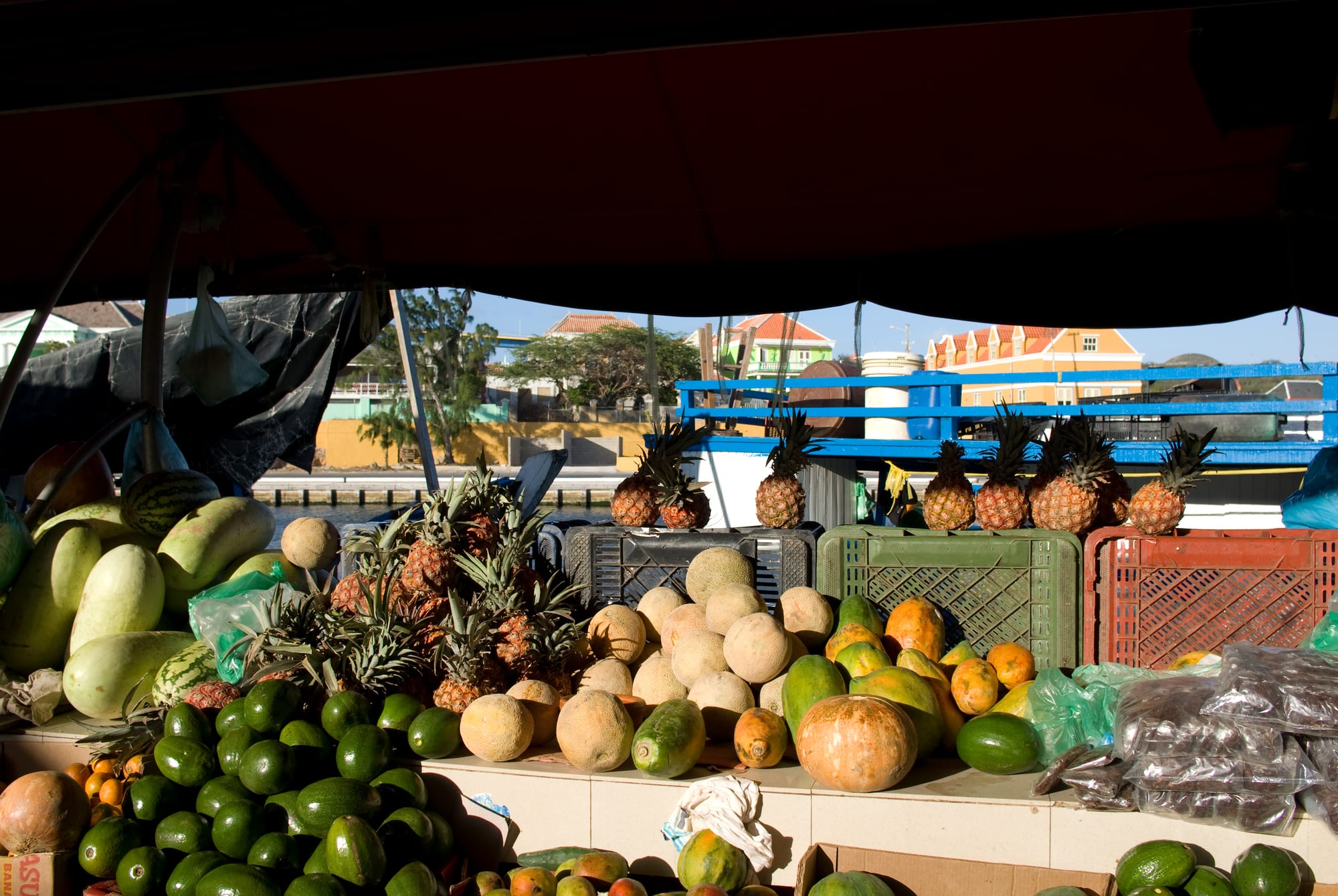 Pineapples, melons, avocados and other fresh produce piled on a market boat moored at the Willemstad waterfront
