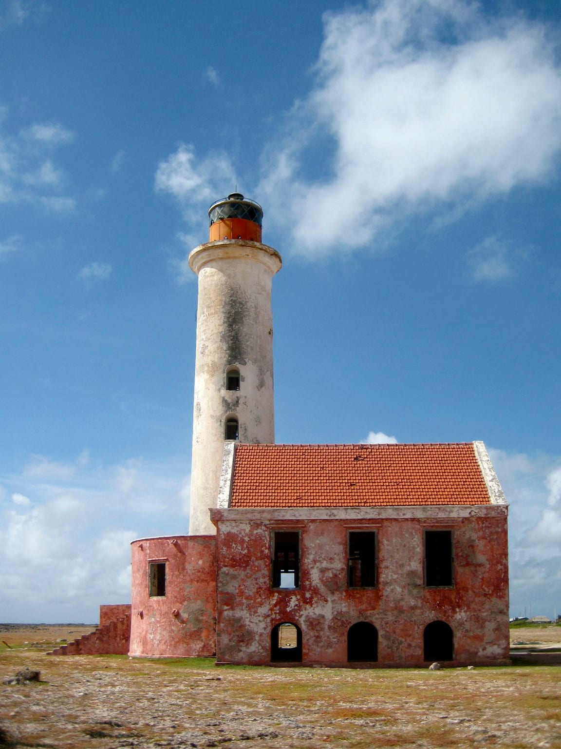 A weathered orange-and-white lighthouse on a low, treeless sandy island under a big sky
