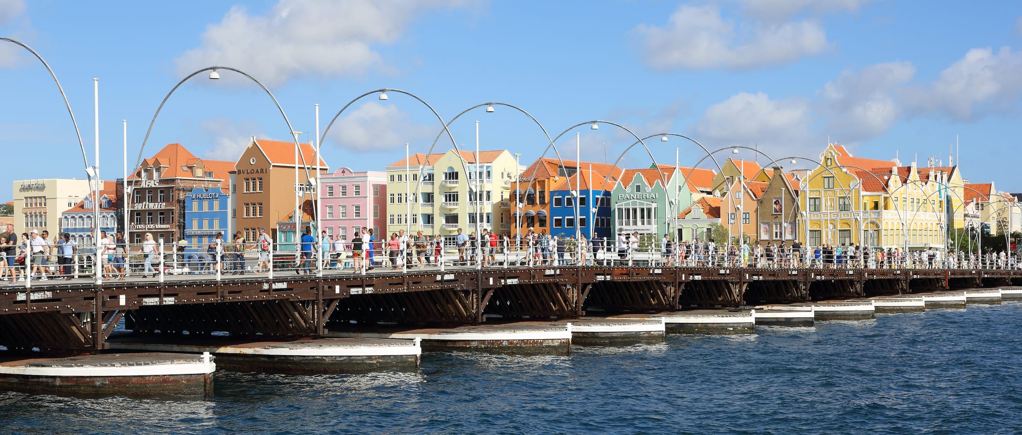 A long pontoon footbridge across a harbour channel, coloured houses behind