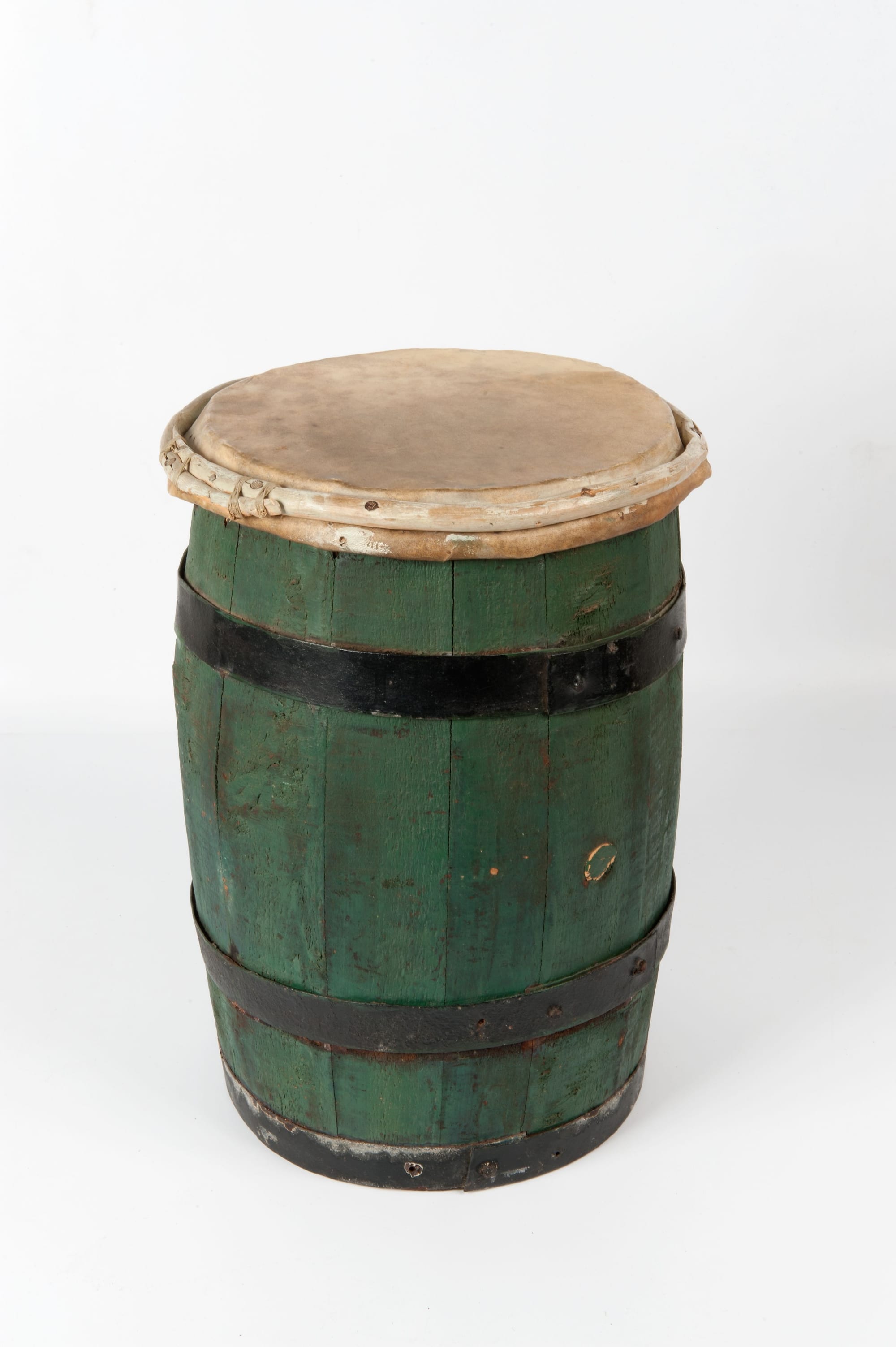 A wooden drum made from a green-painted barrel bound with black iron hoops, with a pale animal-skin head lashed across the top