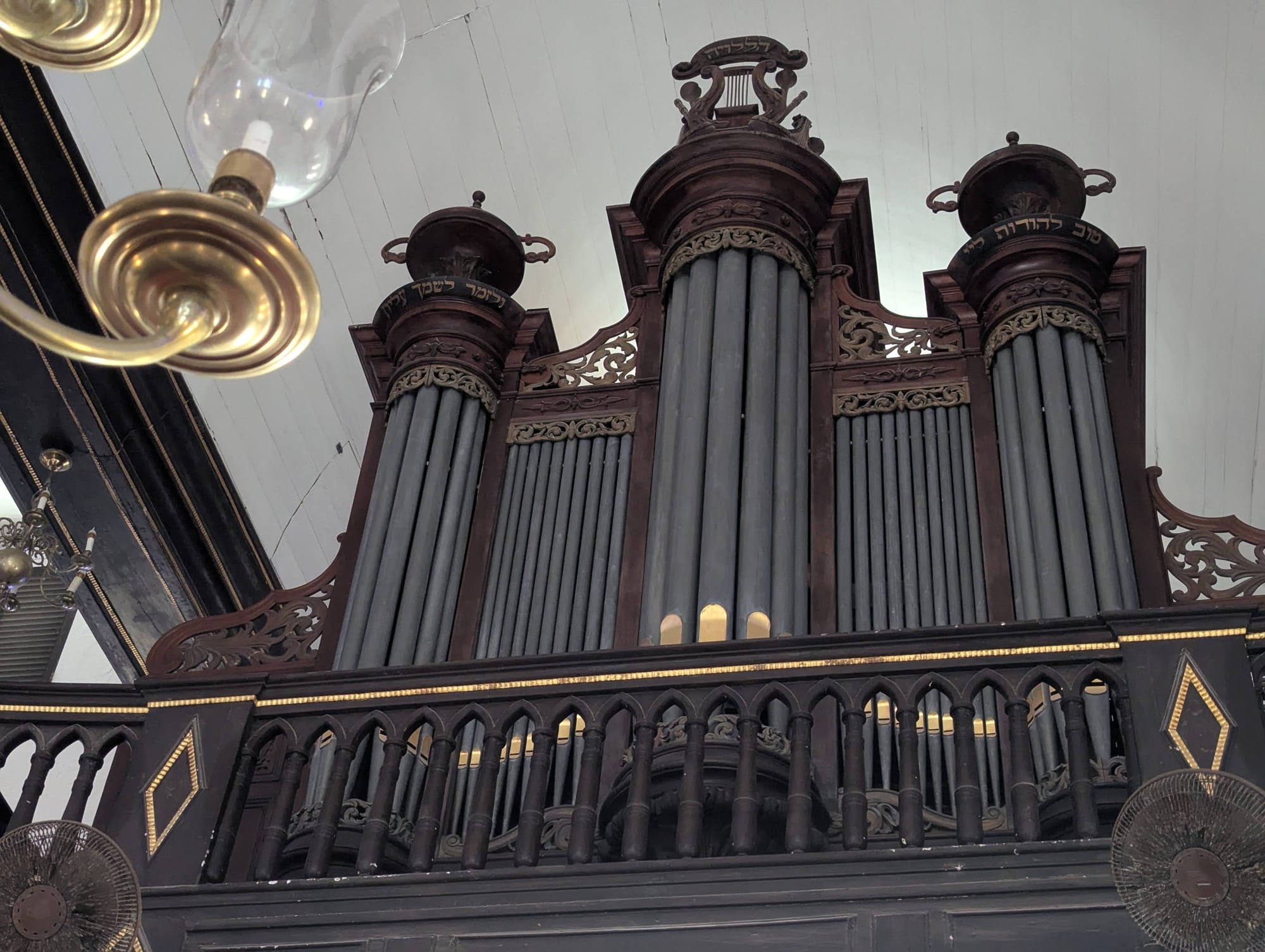 The interior of an 18th-century synagogue with dark wood galleries, brass chandeliers and a sand-covered floor