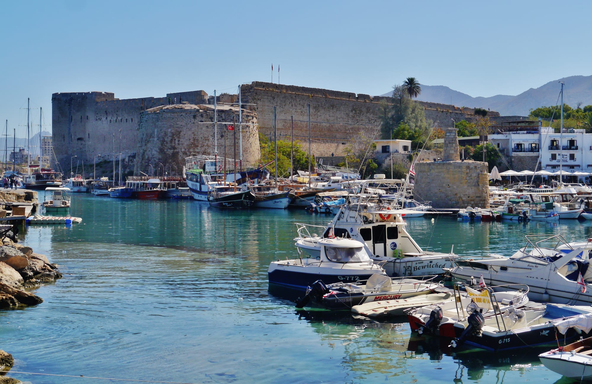 A horseshoe harbour of old stone houses and boats, backed by a large castle and mountains
