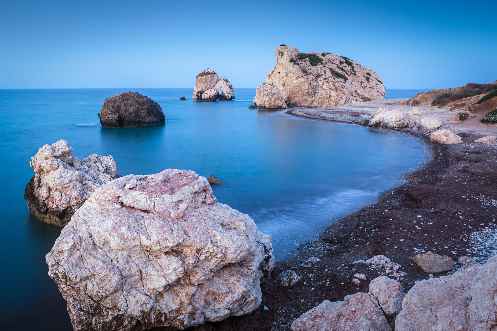 A pebble beach curving toward a large offshore rock, hills behind