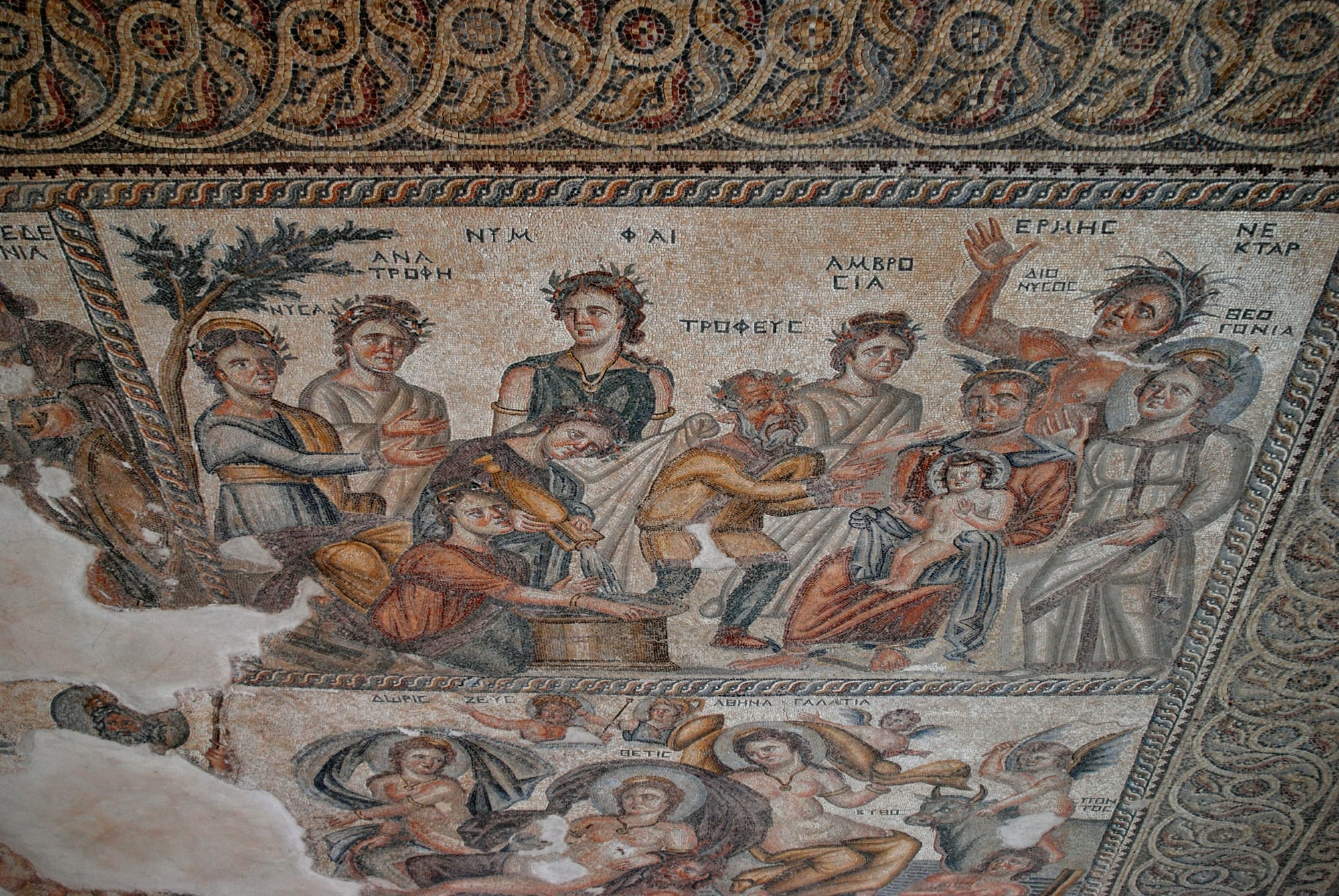 A detailed Roman floor mosaic showing figures around an infant, in reds, golds and greens
