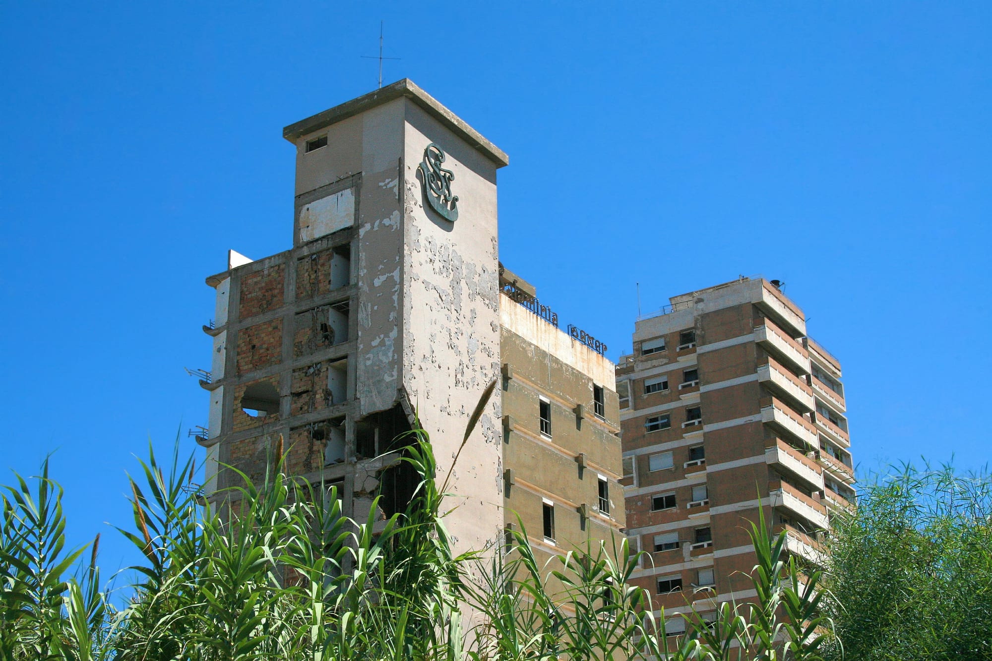 A decaying high-rise beachfront hotel behind a wire fence, its windows empty, on an abandoned coast