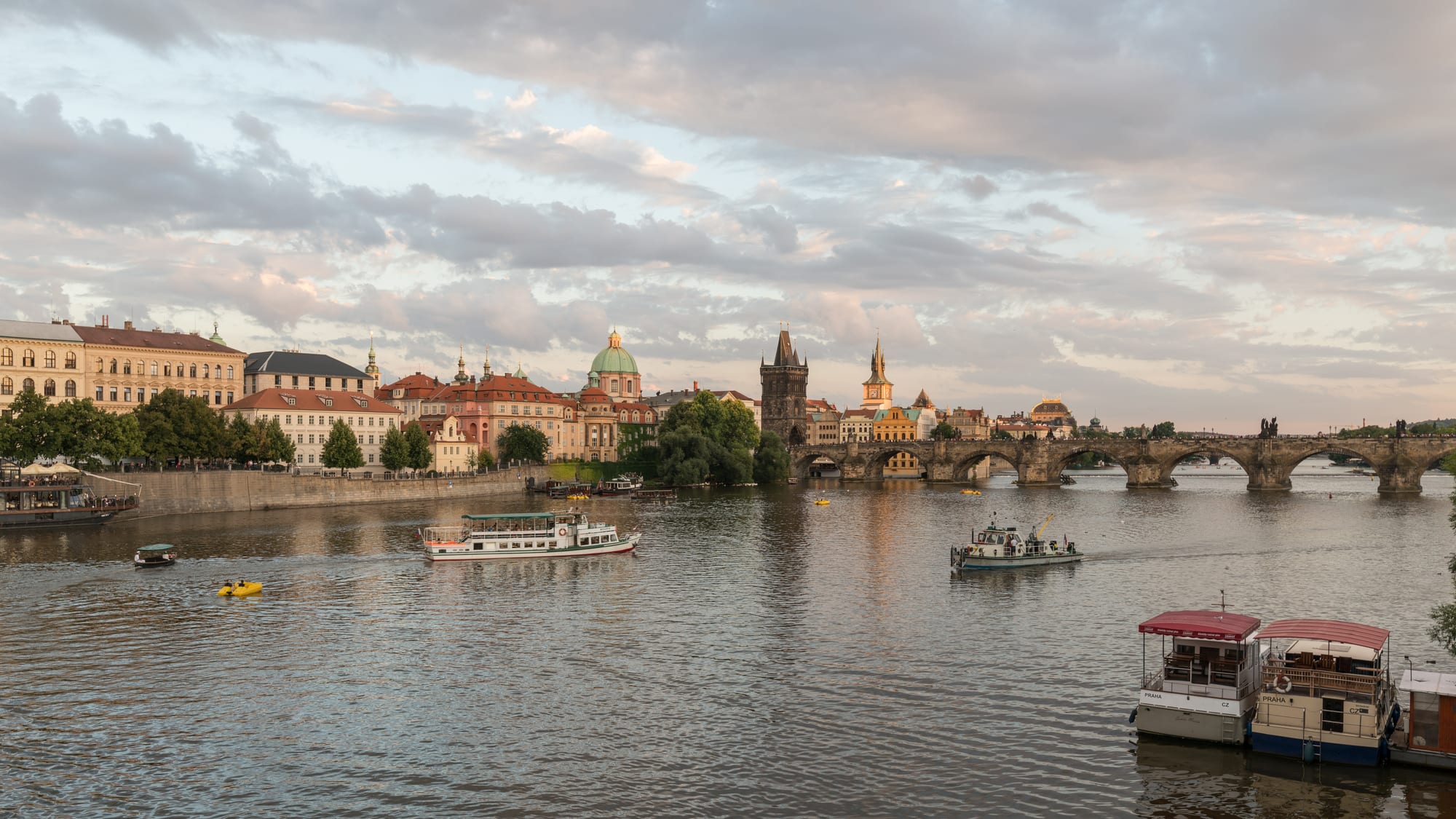 A wide medieval stone bridge lined with statues, a hilltop castle and cathedral rising behind