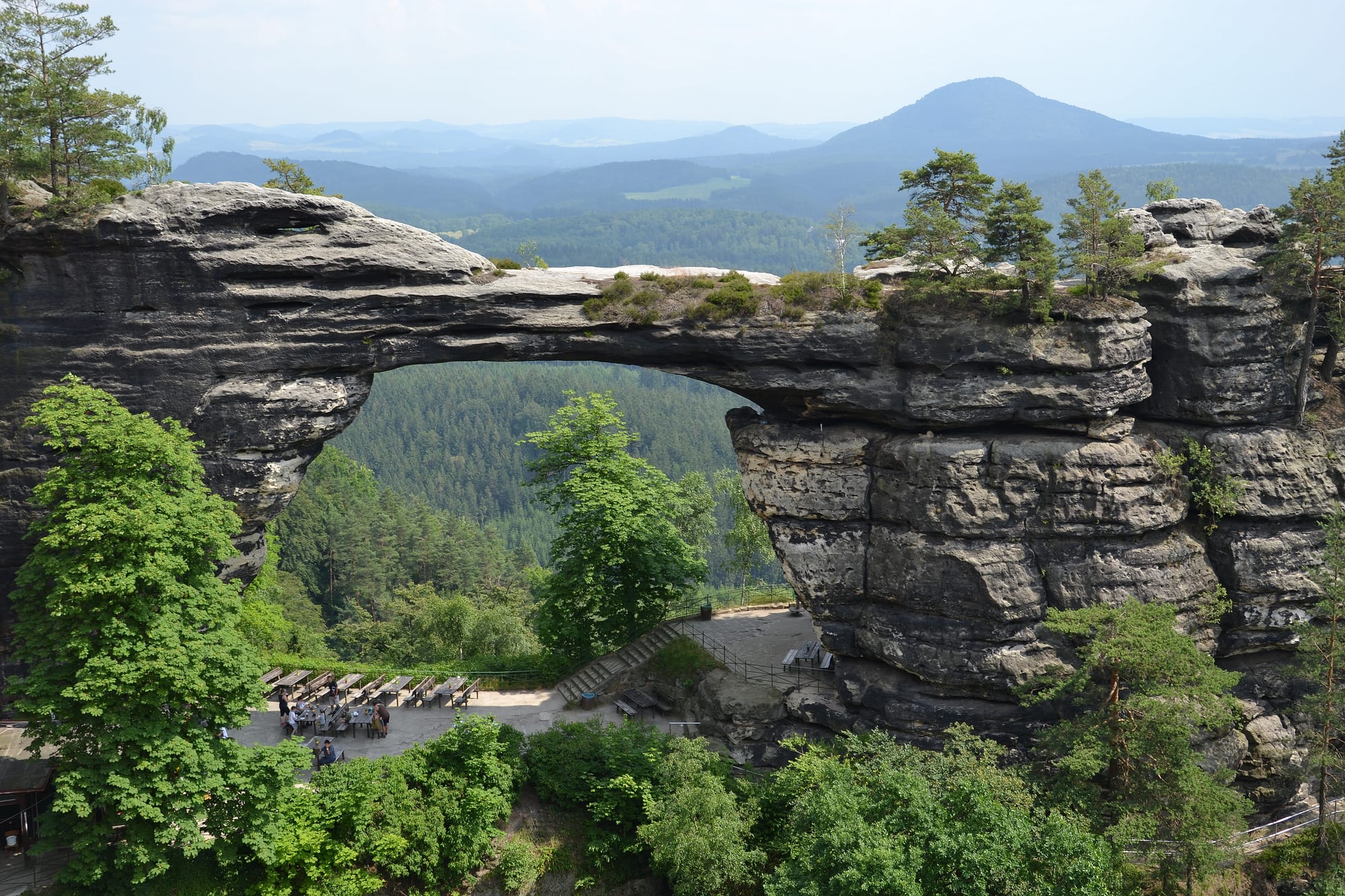 A large natural sandstone arch spanning a gap between forested rock towers