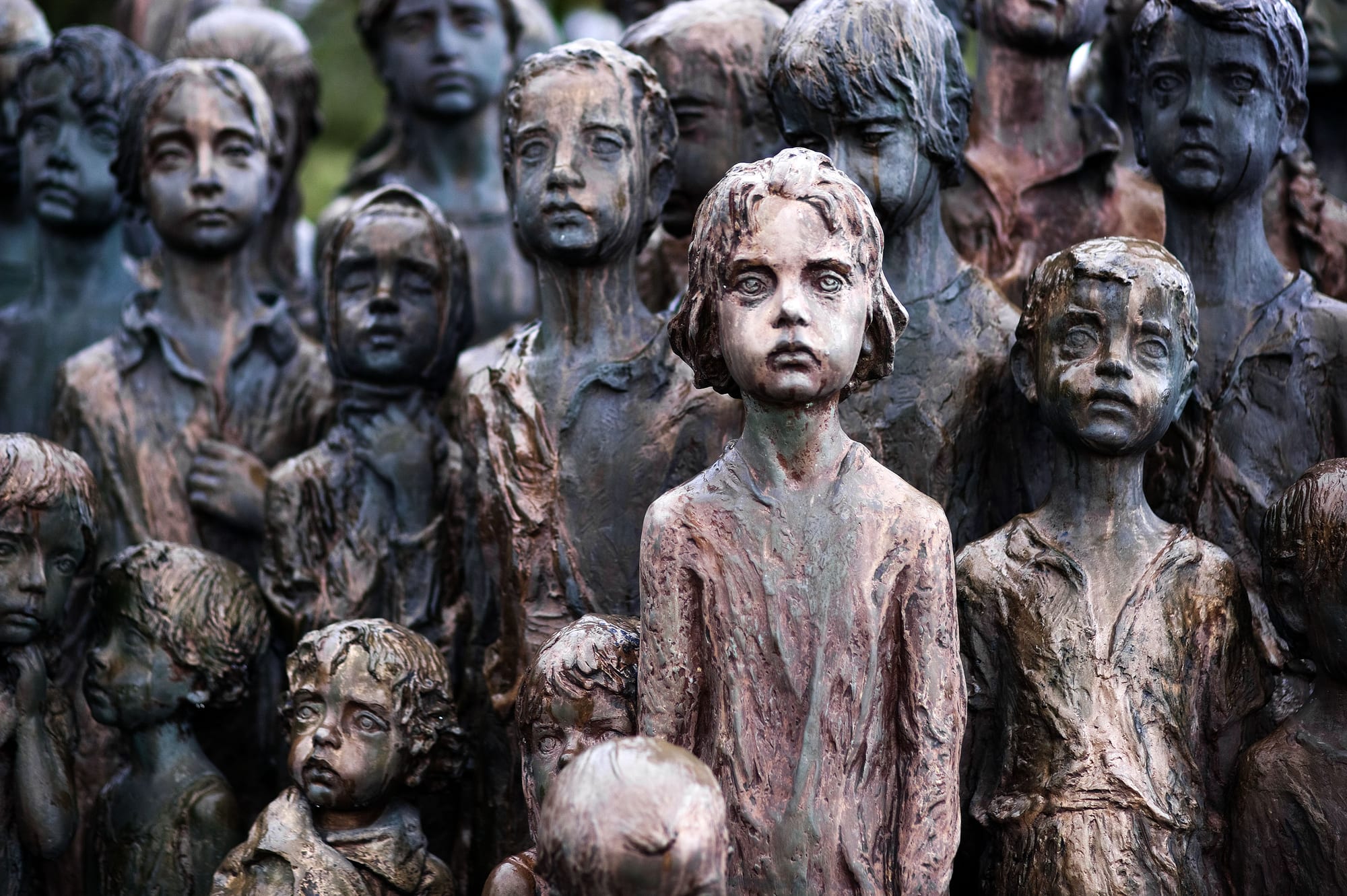A bronze sculpture group of children's figures standing in a green field where a village once stood
