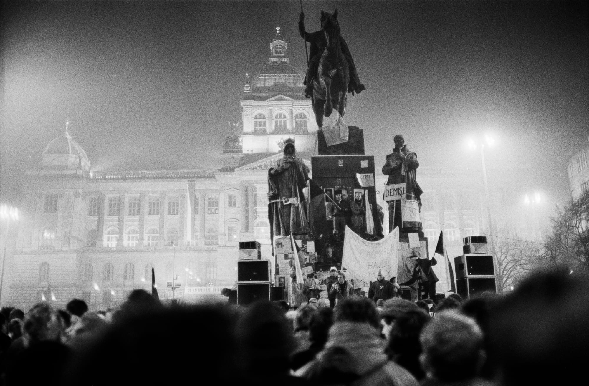 A vast night-time crowd filling a long boulevard, many holding lit candles and flags