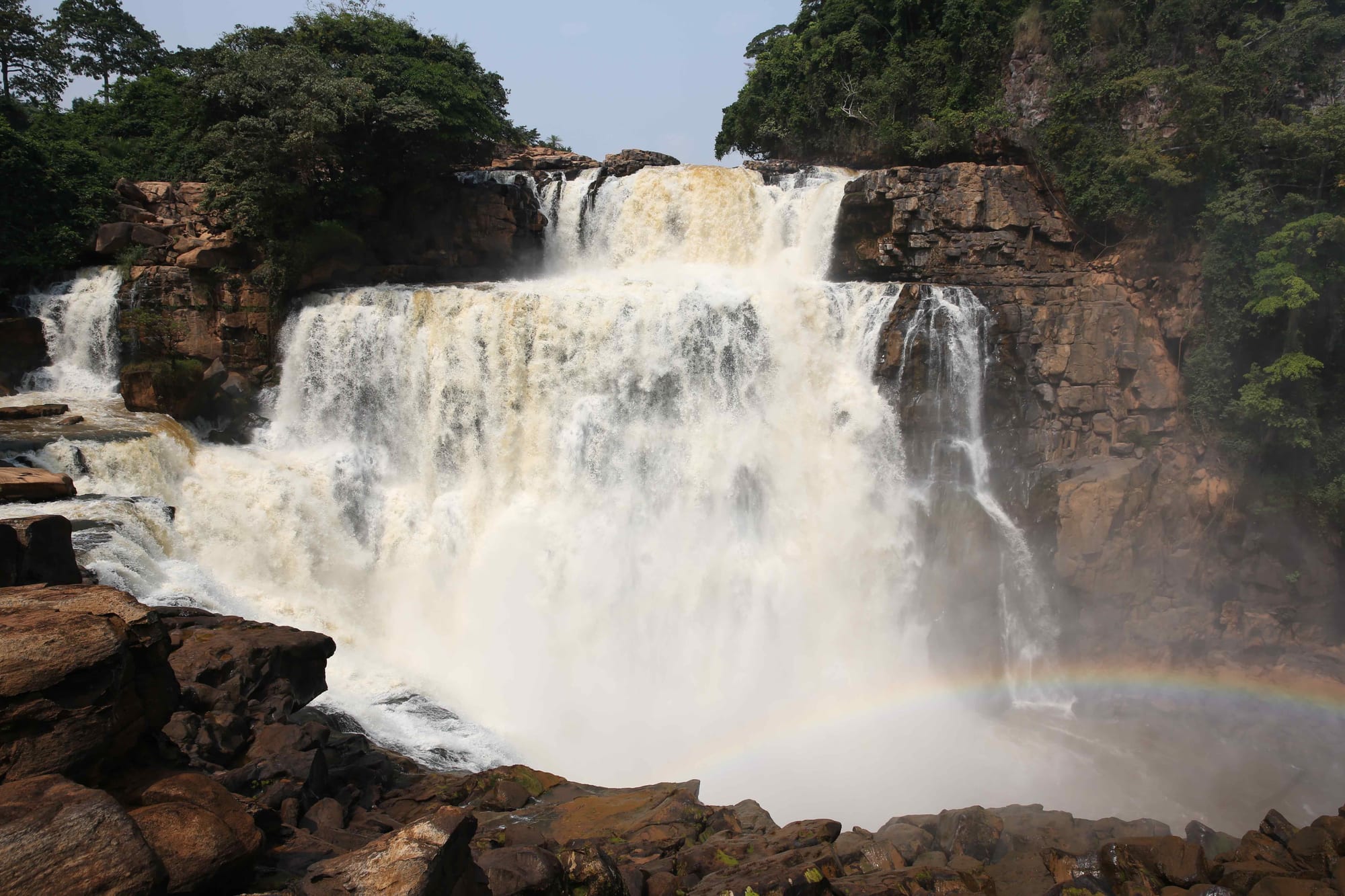 A powerful waterfall crashing over a rock face into a misty gorge surrounded by forest
