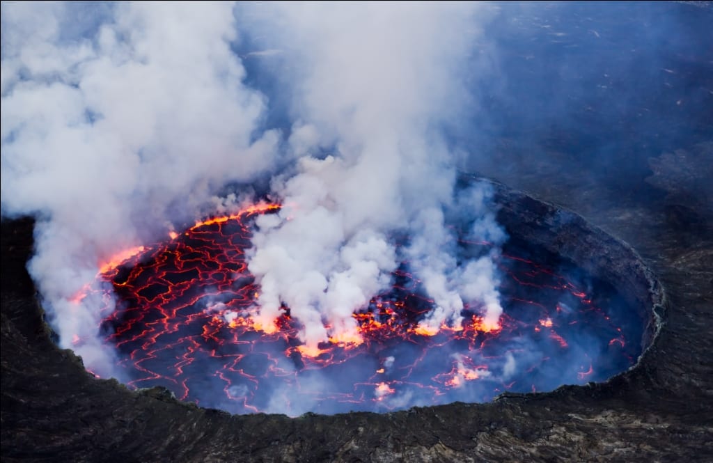 A churning orange lake of molten lava at the bottom of a huge dark crater at night