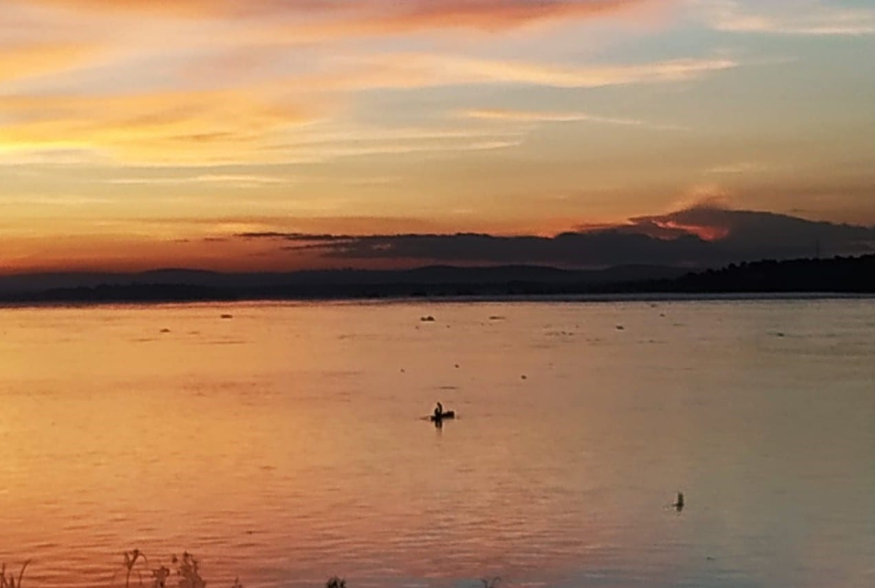 A vast river at sunset with silhouetted boats and a wide, glowing horizon