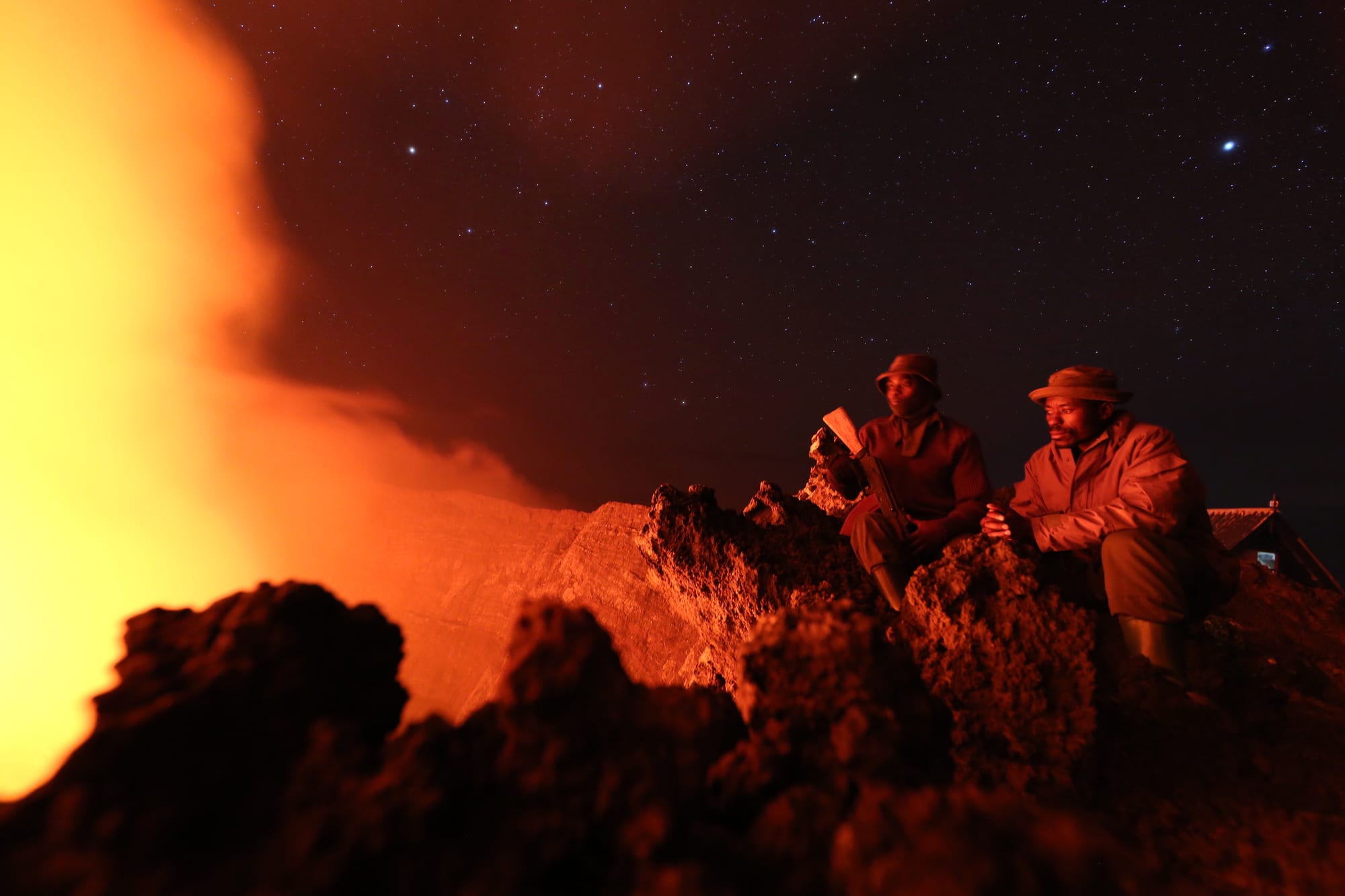 Two park rangers silhouetted on a crater rim above a glowing lava lake