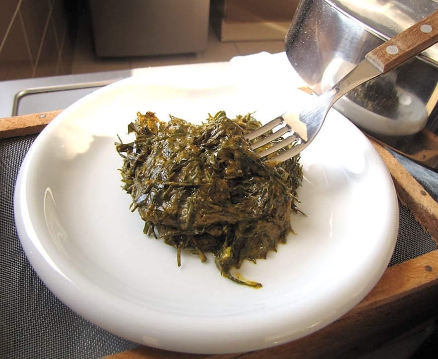 A bowl of finely chopped dark green leaves in a peanut sauce