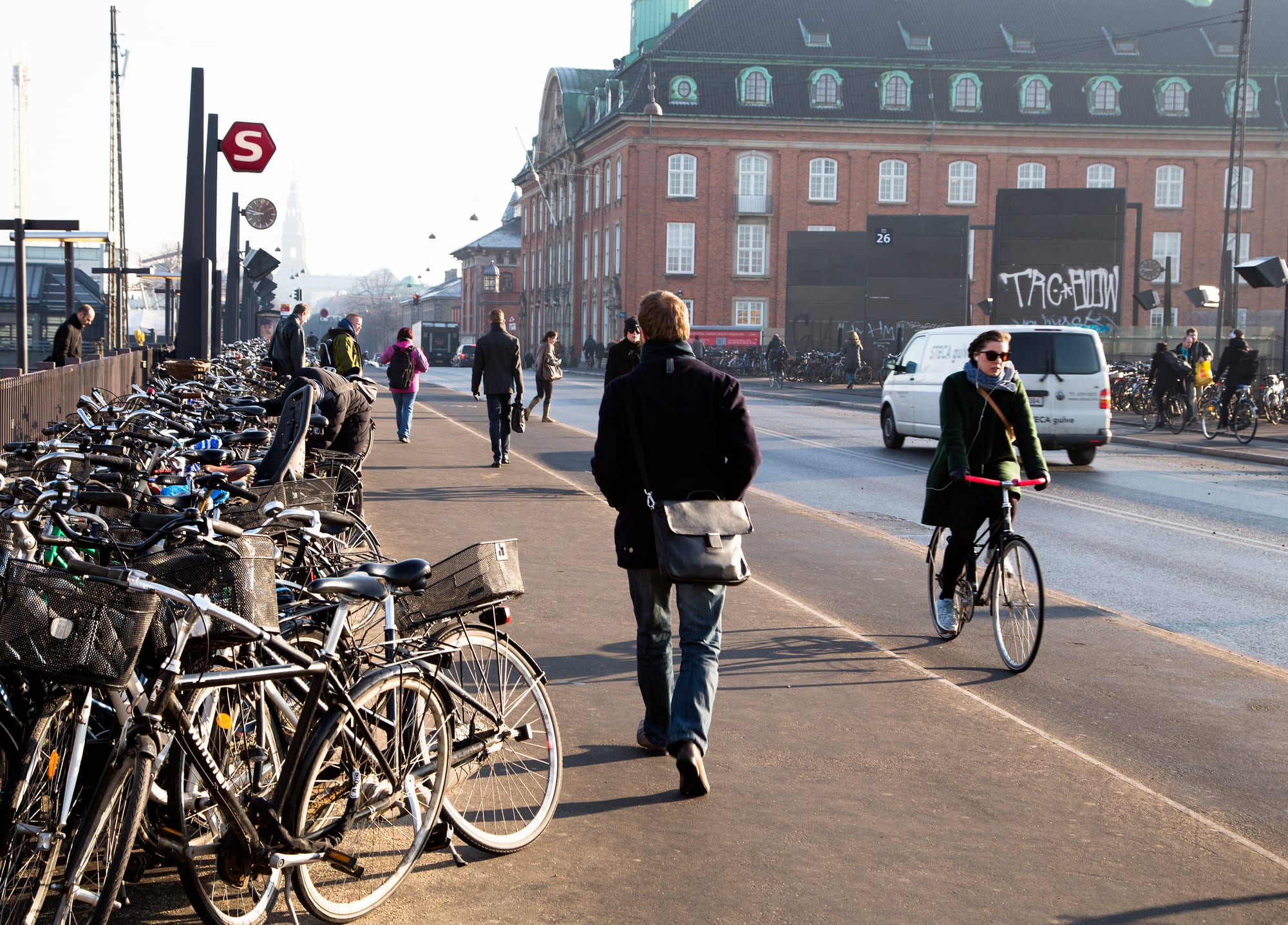Rows of parked bicycles lining a street outside Copenhagen's central railway station, with cyclists and pedestrians passing by