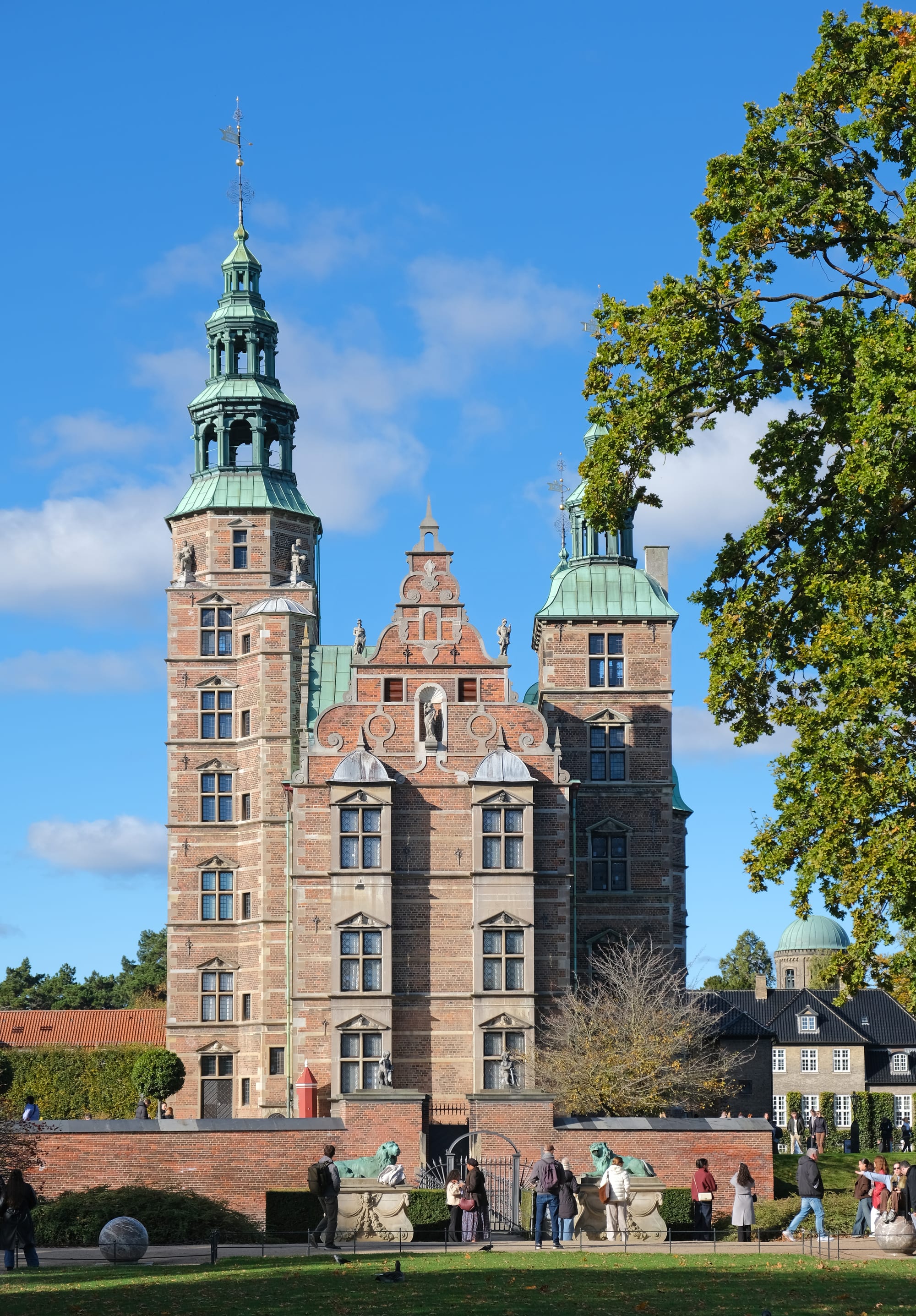 A red-brick Renaissance castle with copper-green spires, in a formal garden