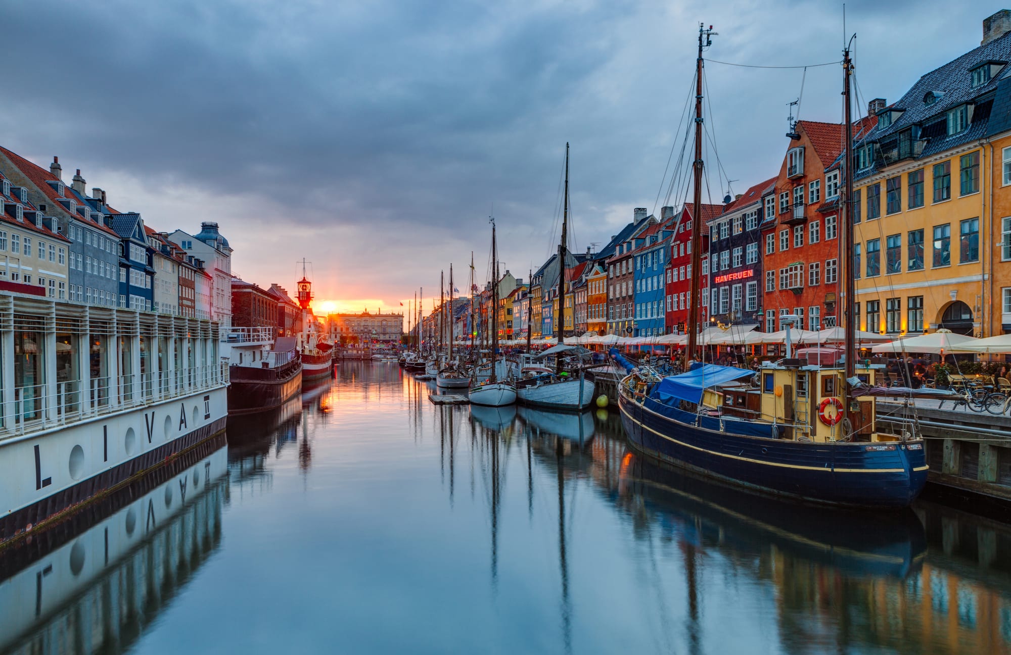Coloured harbour houses glowing at sunset, boats and diners in the foreground